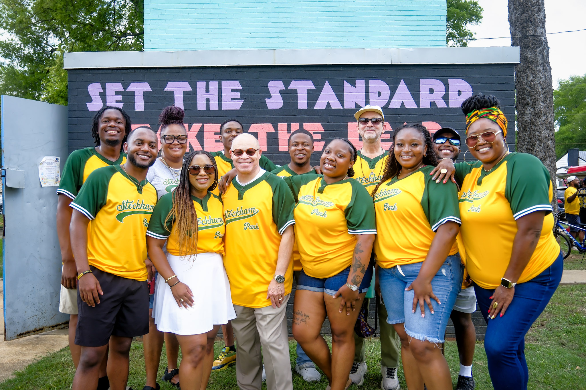 Group of people standing outdoors in front of a sign that reads 'Set the Standard,' smiling and posing for a photo.