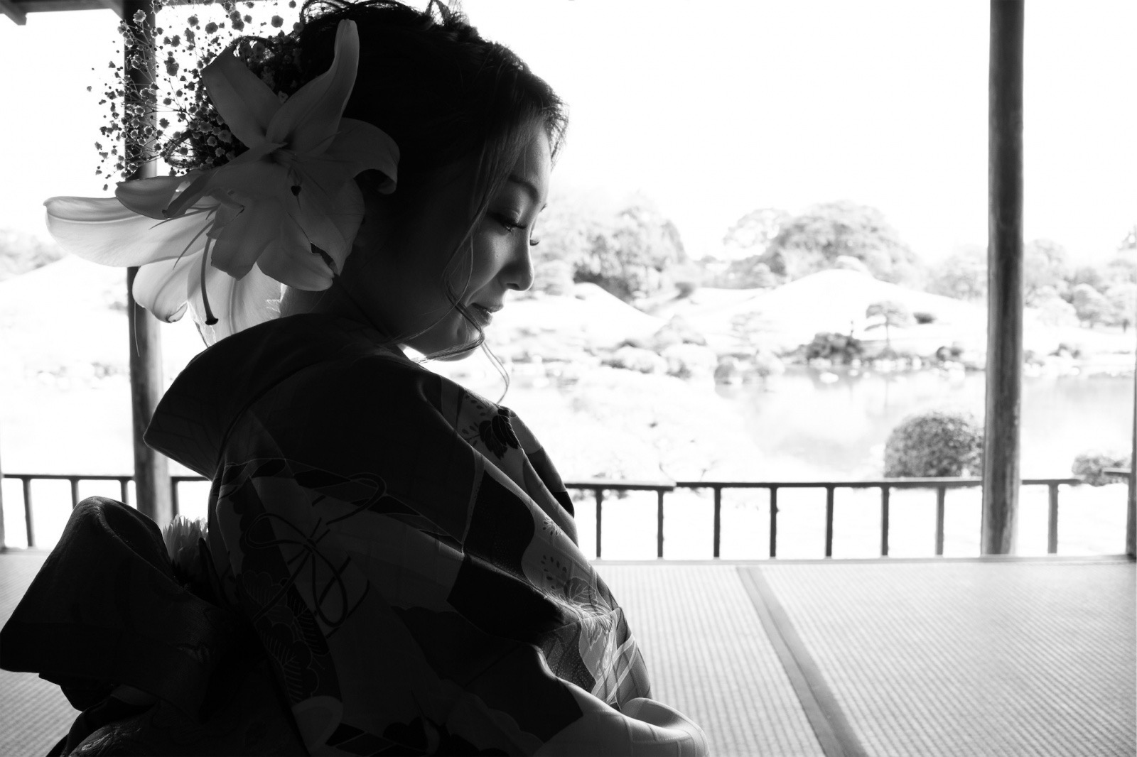 Young woman in traditional attire sitting indoors, looking out a window at a landscape, with a large bow in her hair.