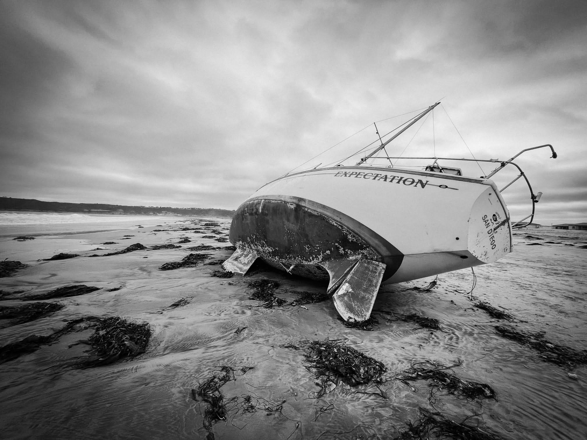 Sailboat stranded on a beach with a cloudy sky in the background.