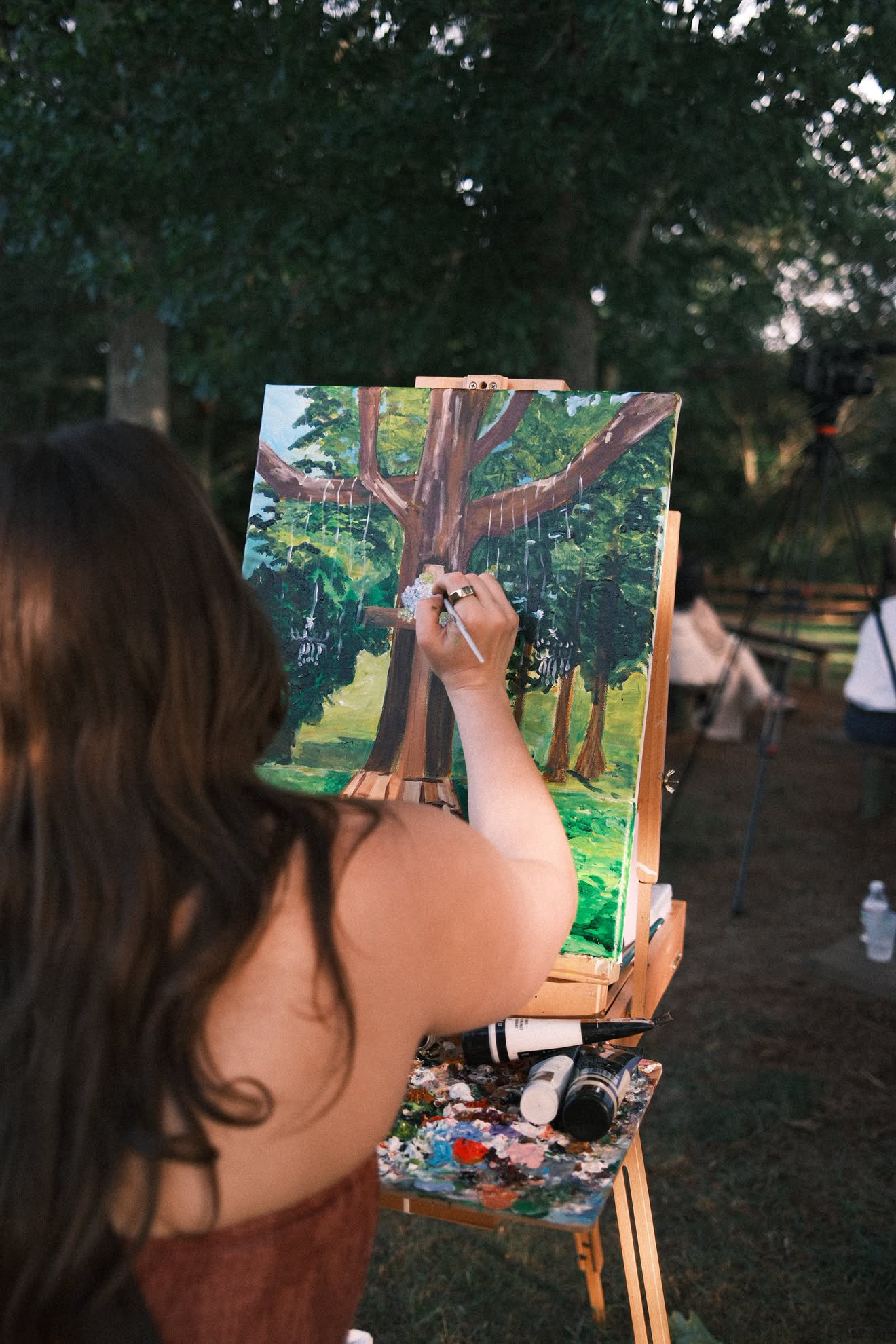 Person painting a large tree on an outdoor canvas with a park background.