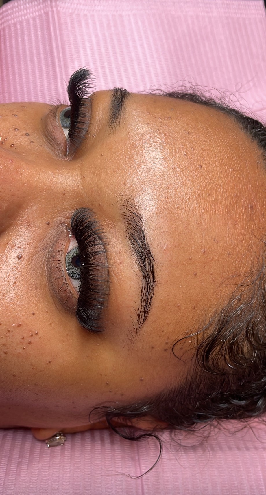 Close-up of a woman's face with makeup, lying on a pink surface, showing her eyes and eyebrows.