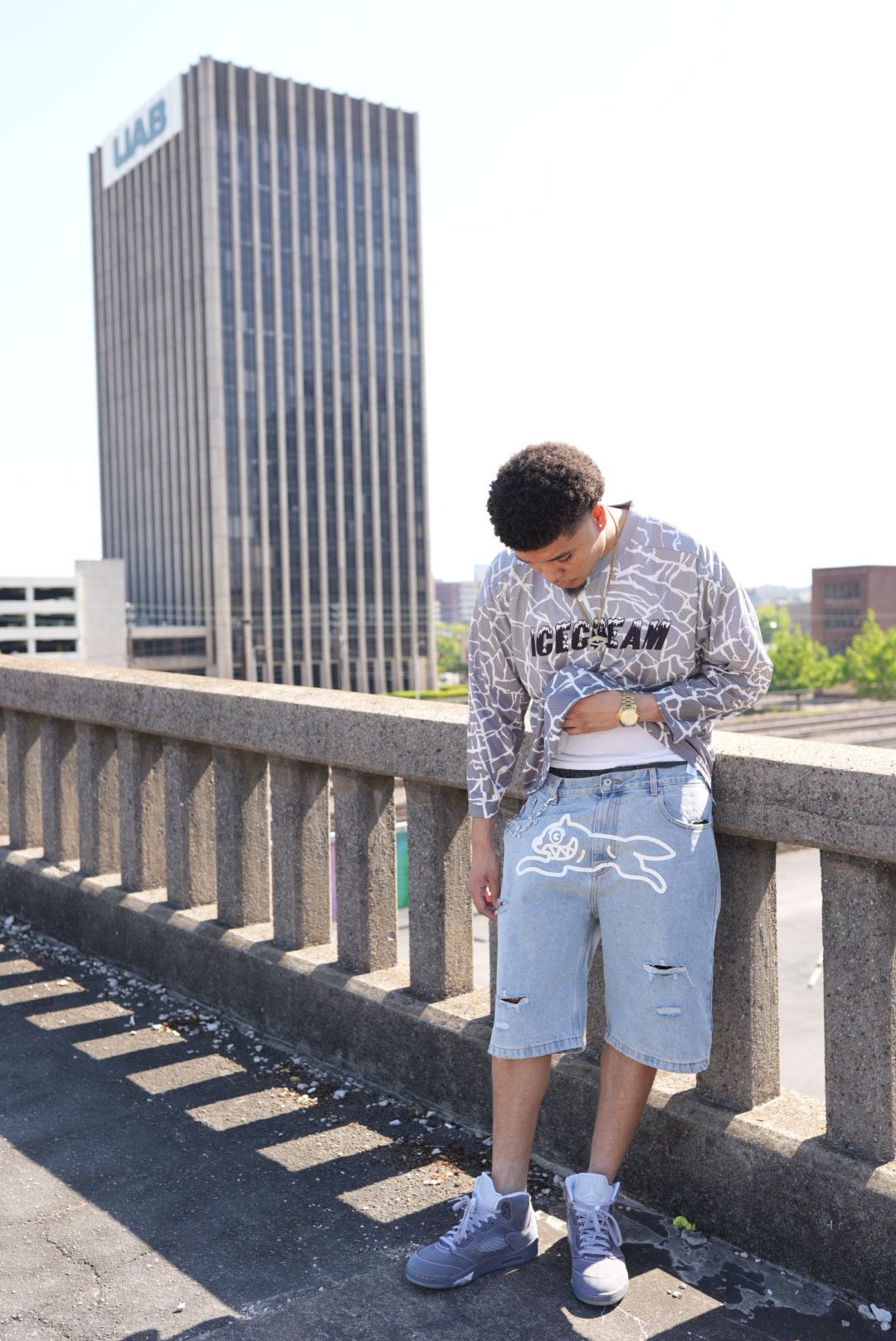 Person standing on a bridge railing, facing away, with tall buildings in the background.