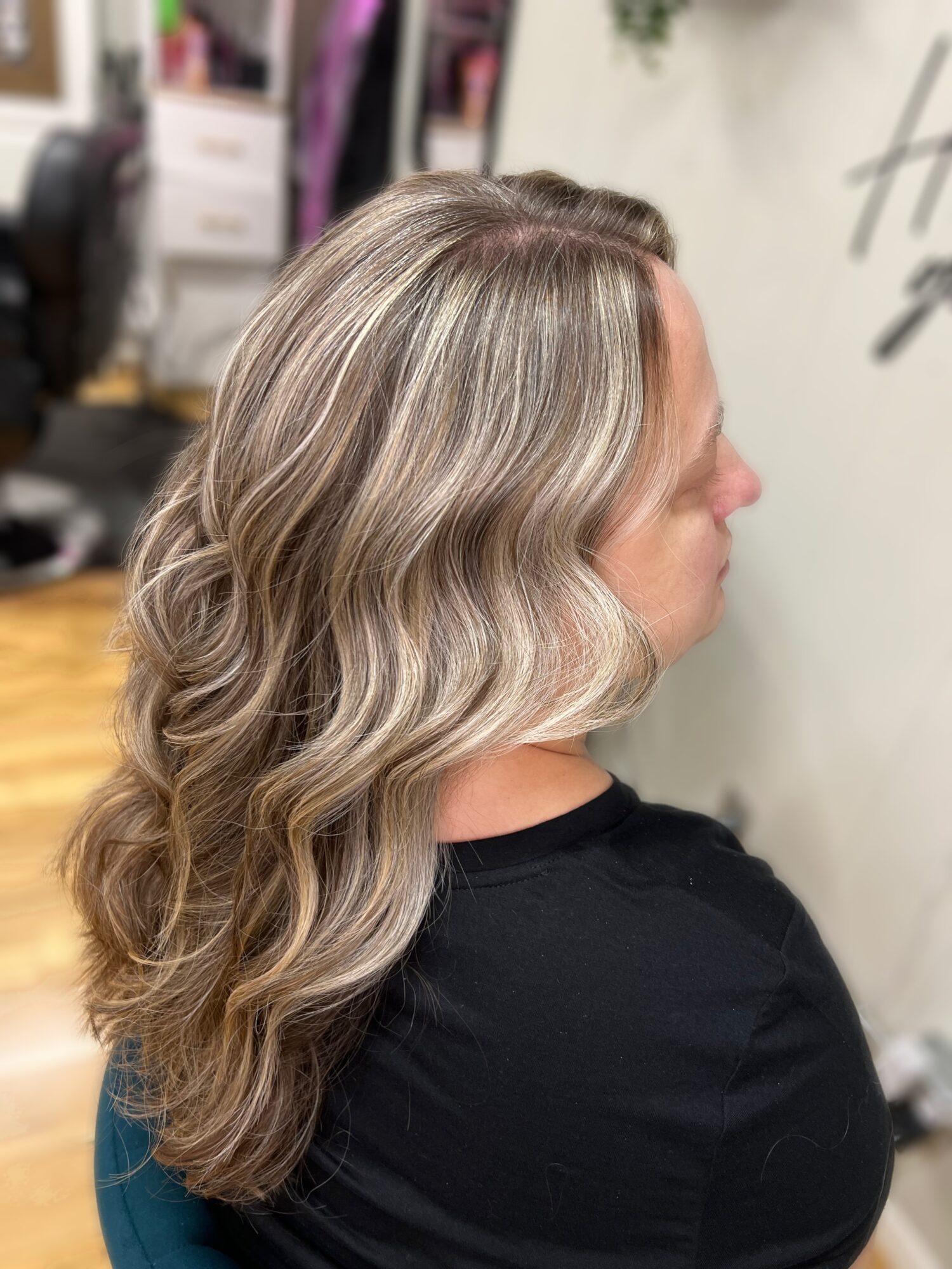 Side view of a woman with long, wavy blonde hair, wearing a black top, in an indoor setting.
