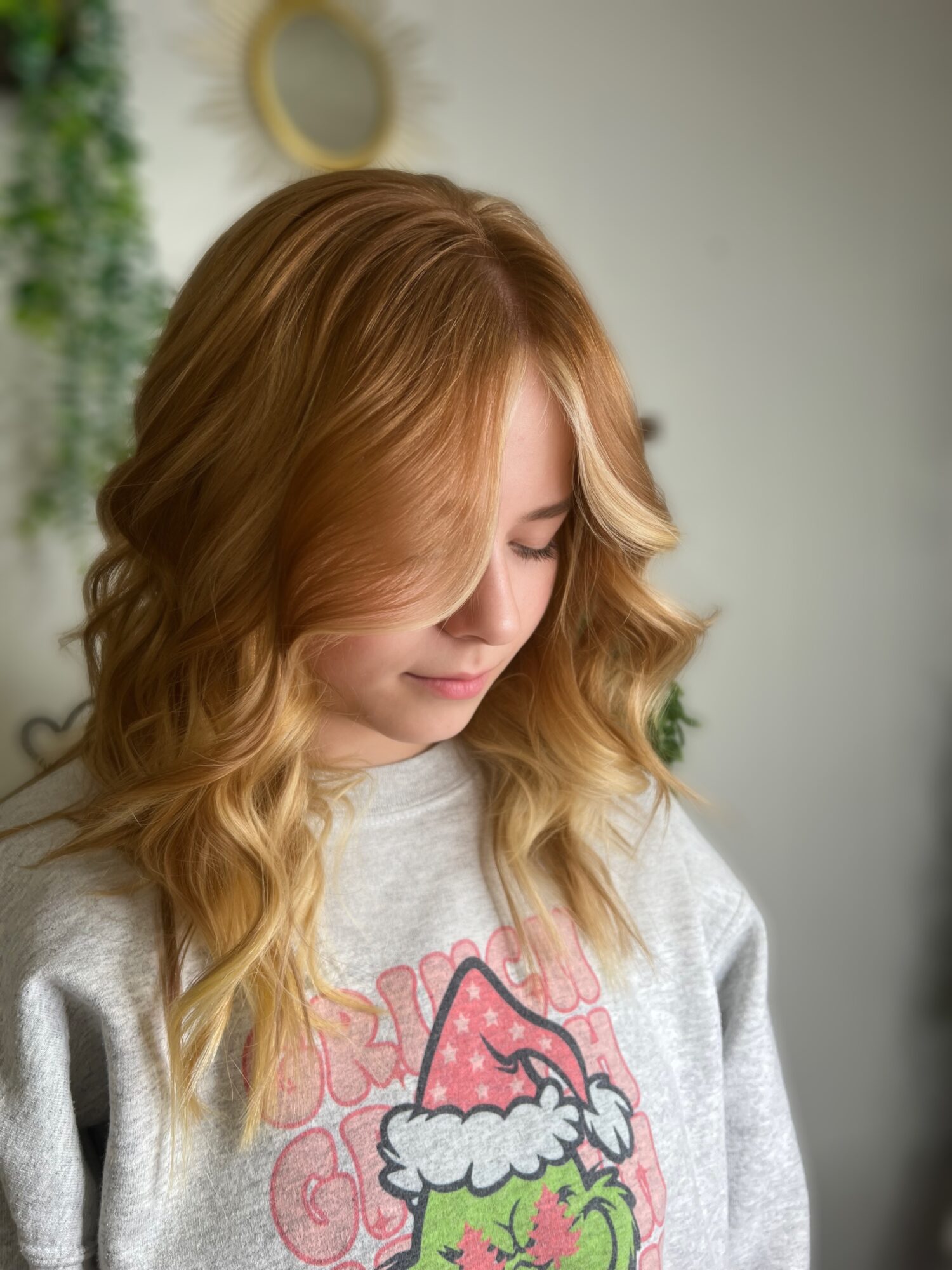 Young woman with wavy blonde hair looking downward, wearing a gray sweatshirt with a Christmas-themed graphic.