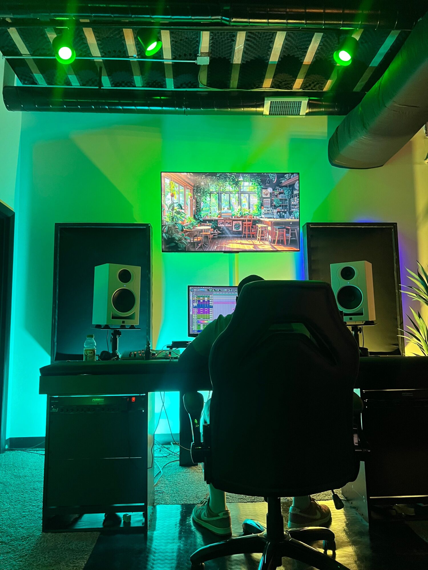 Recording studio with monitors, equipment, and colorful lighting, viewed from a seated perspective.