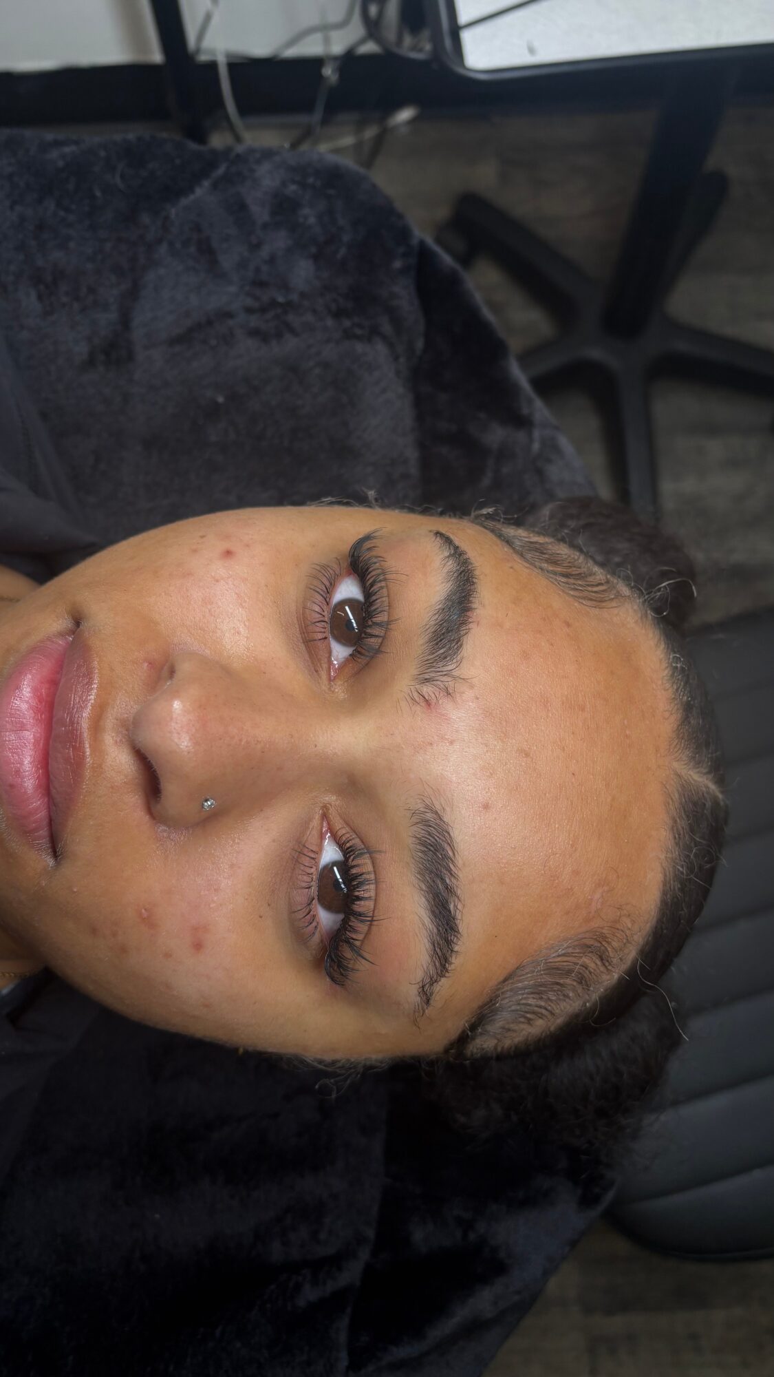Close-up of a woman's face with makeup, lying down on a black surface, with a blurred background.