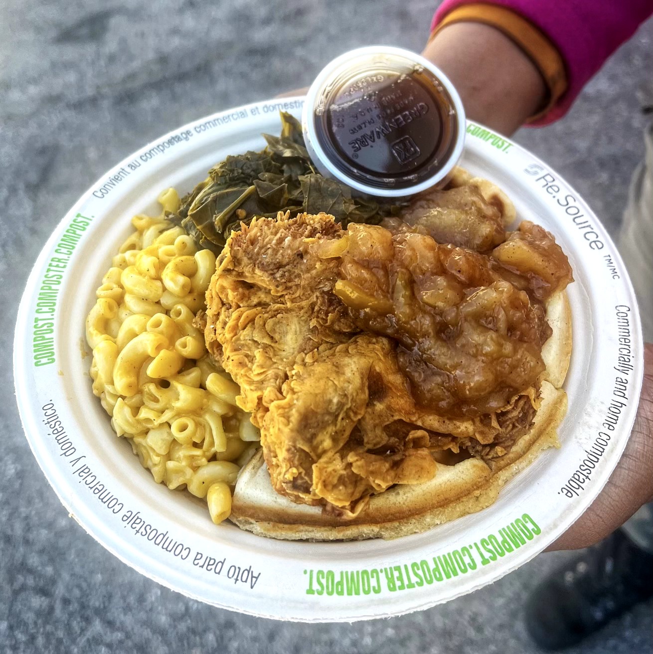 Plate with macaroni, fried chicken, gravy, and a cup of dark beverage, held by a person wearing a pink sleeve.
