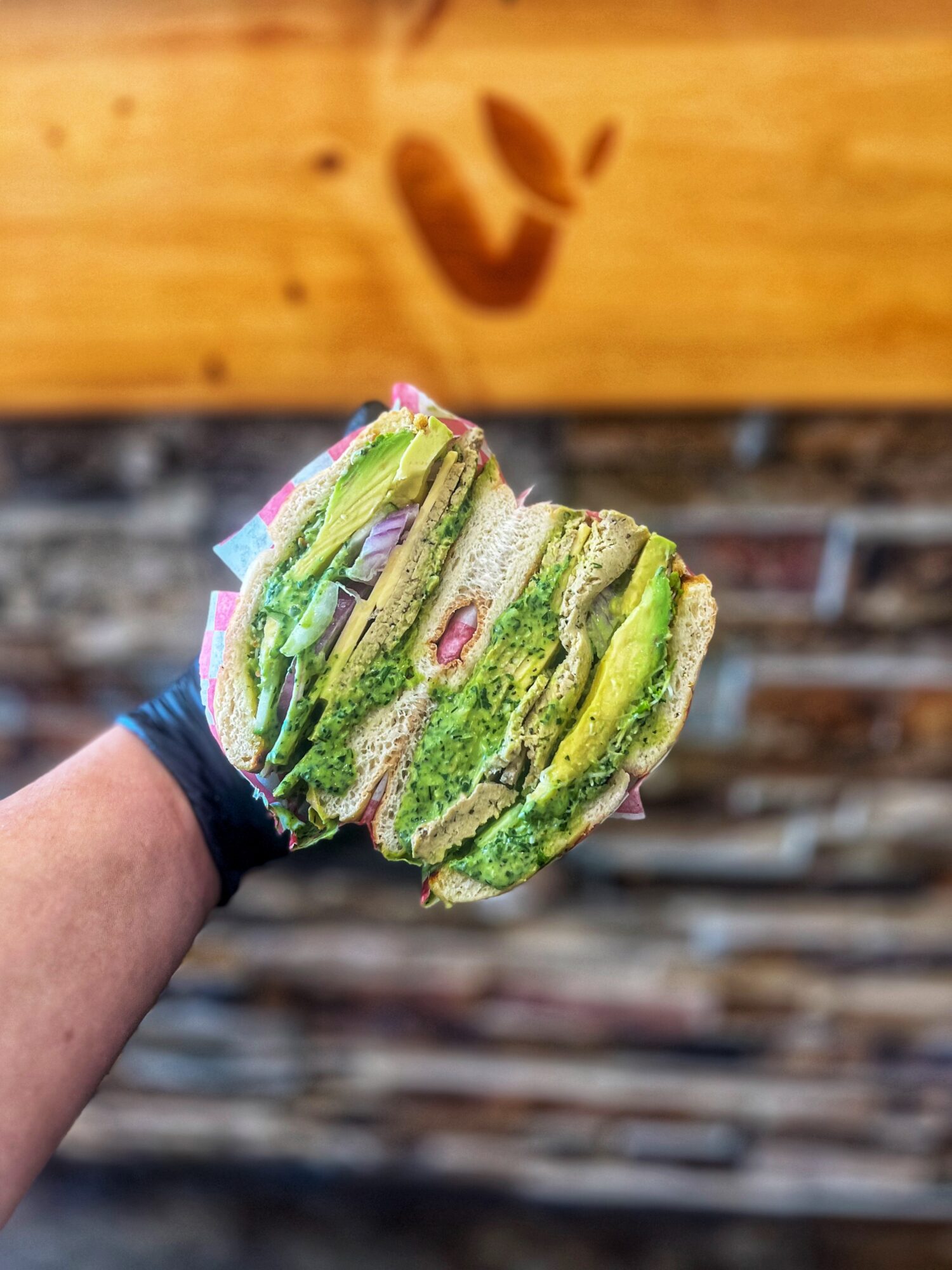 Hand holding a green layered cake with pink decorations, background of wooden and brick wall.