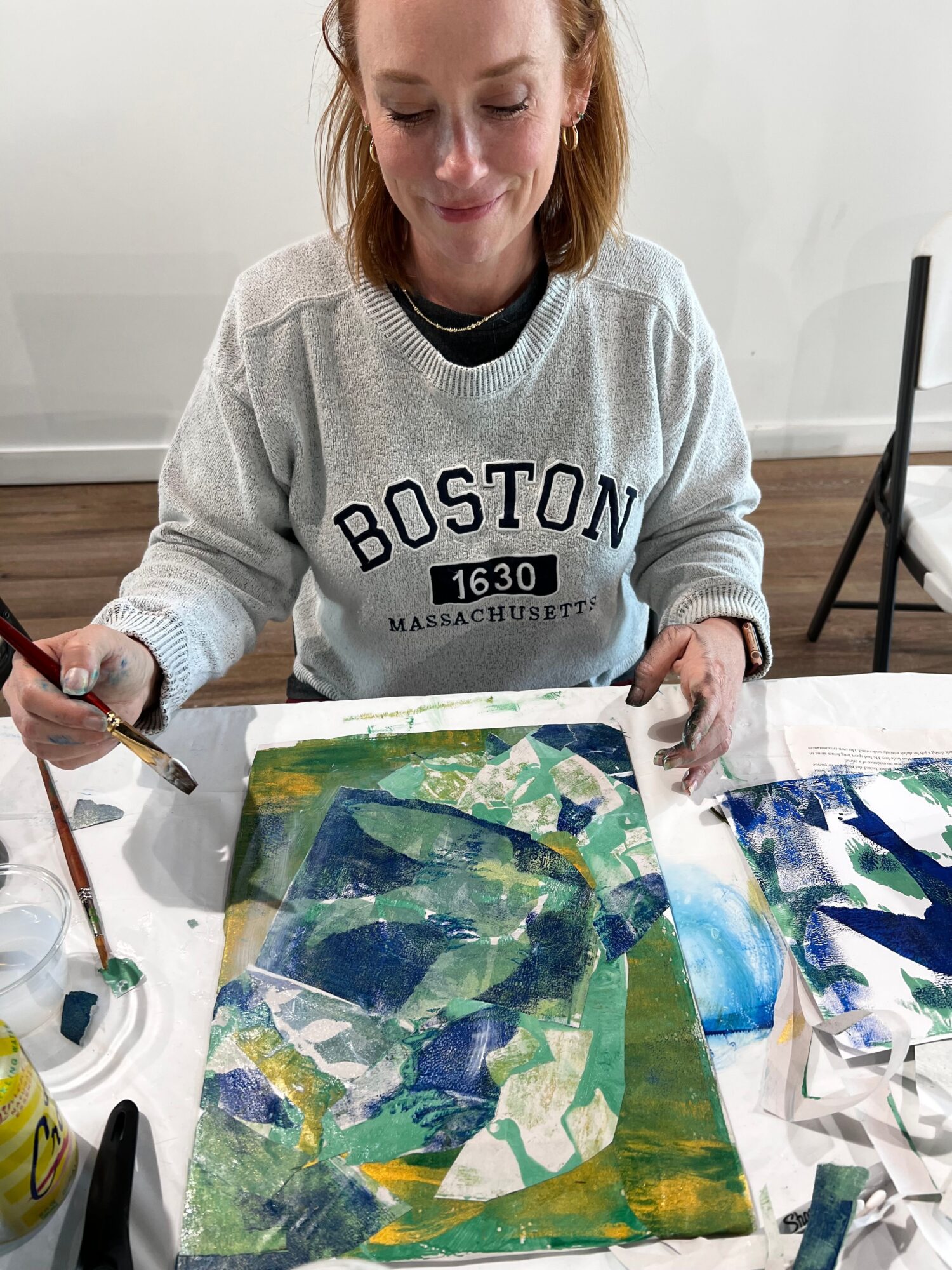 Person painting an abstract artwork with blue, green, and yellow colors on a canvas.