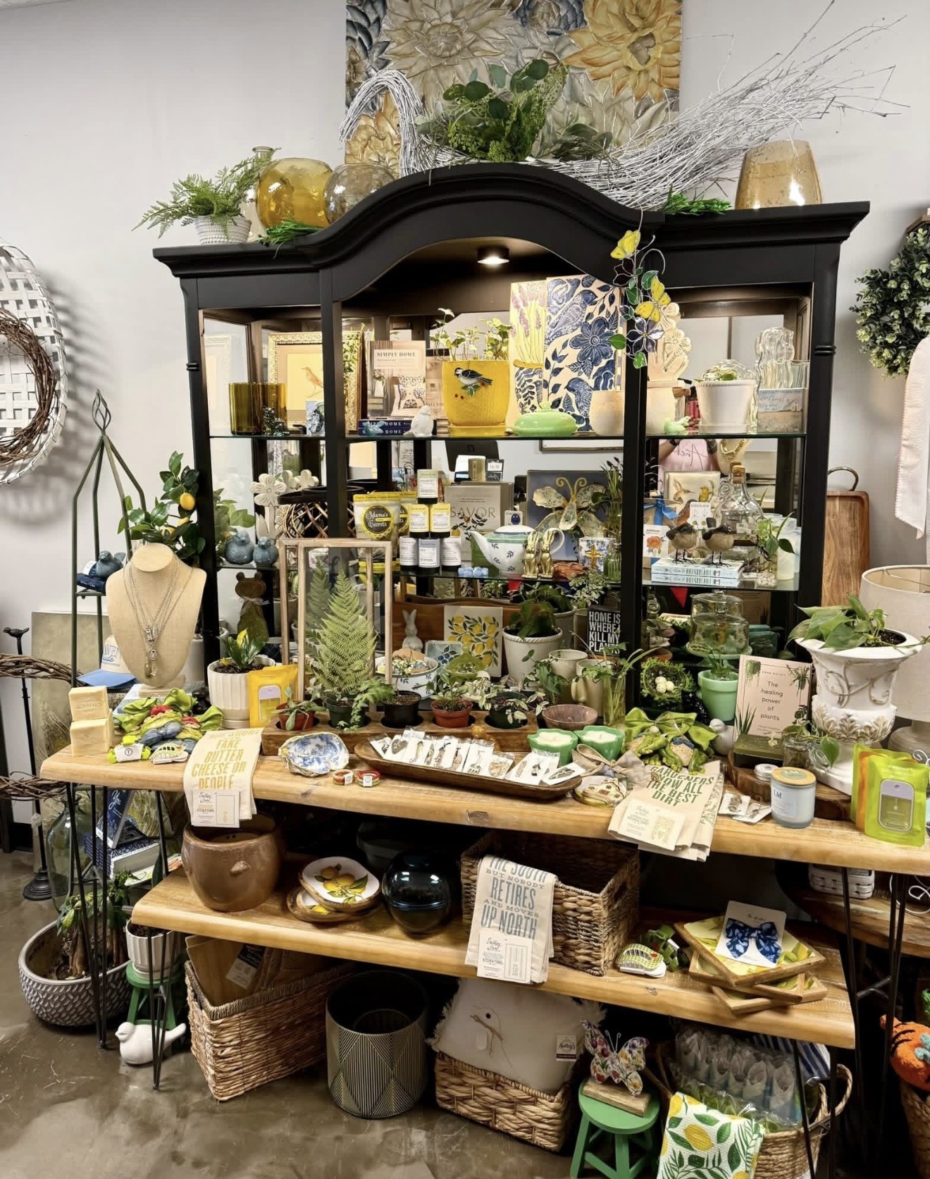 Display cabinet filled with decorative items, plants, and small gifts, with tables holding additional items in front.