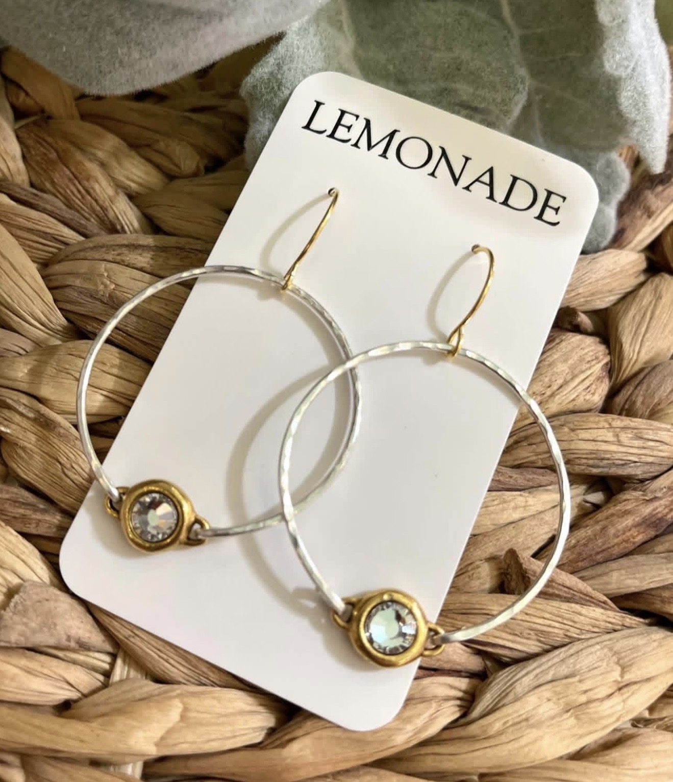 Pair of hoop earrings with gold accents and clear stones on a white card labeled 'LEMONADE', placed on woven surface.
