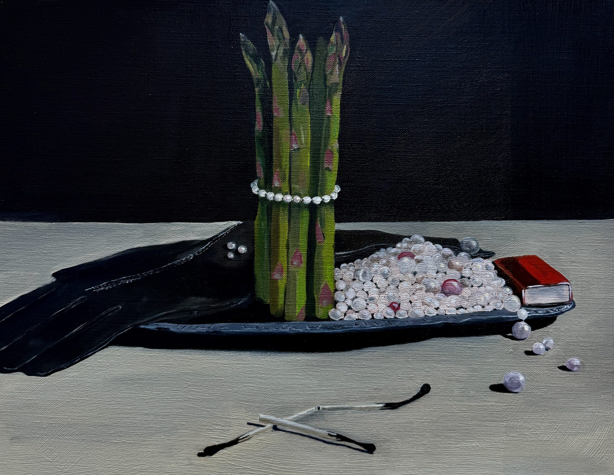 A black tray holds asparagus with a pearl necklace, white beads, a red object, and a pair of glasses on a white surface.