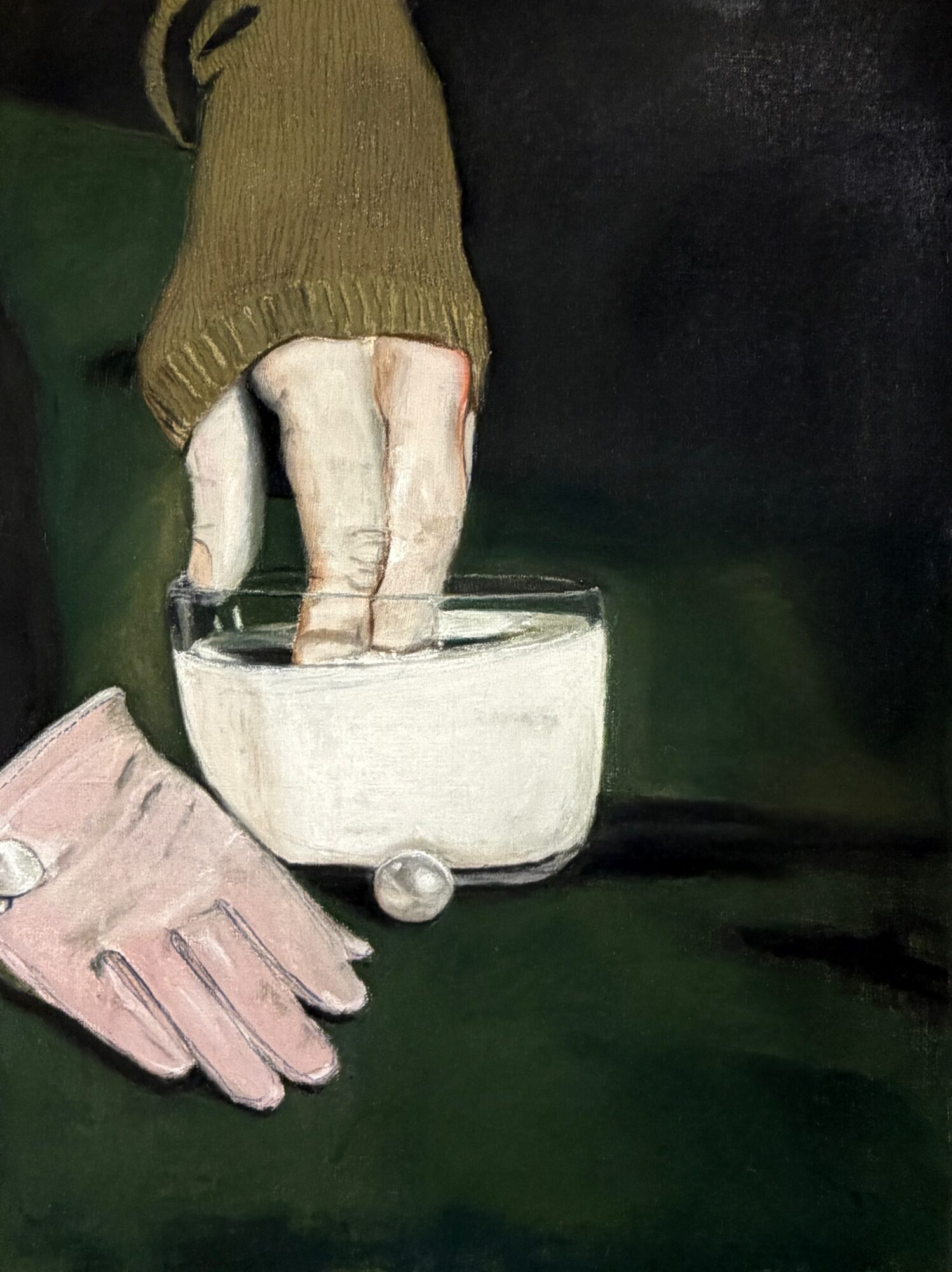 Two hands, one in a pink glove and the other in a green sleeve, are touching a glass container on a dark surface.