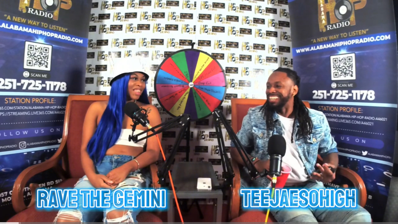 Two people sit in a radio studio with a colorful spinning wheel behind them, smiling and talking into microphones.