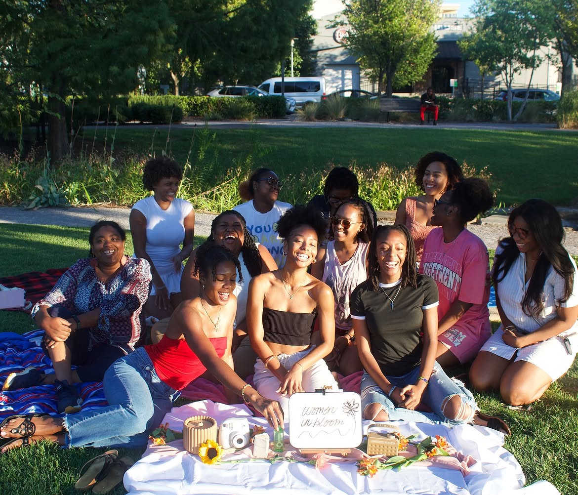 Group of children and teenagers sitting on grass outdoors with a white cloth and items in front, smiling.