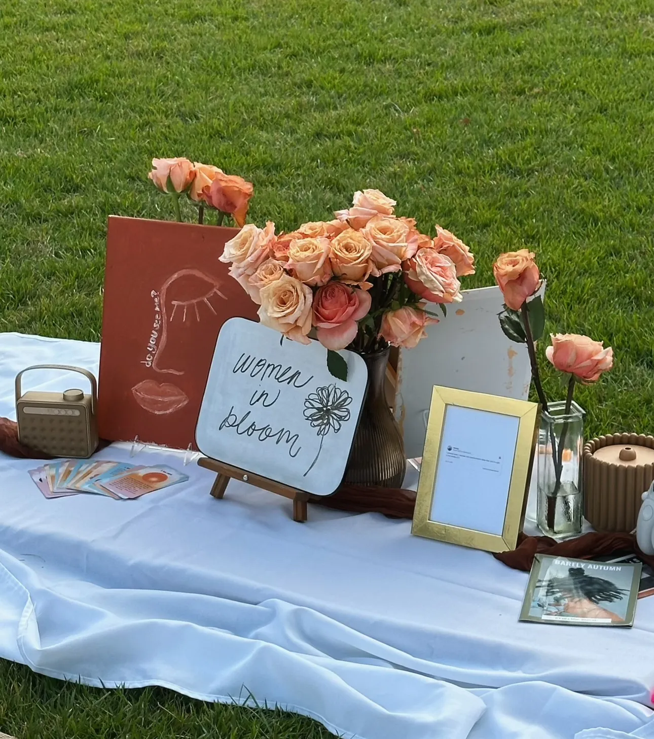 Flowers, framed photos, and decorative items arranged on a white cloth outdoors, with a grassy background.