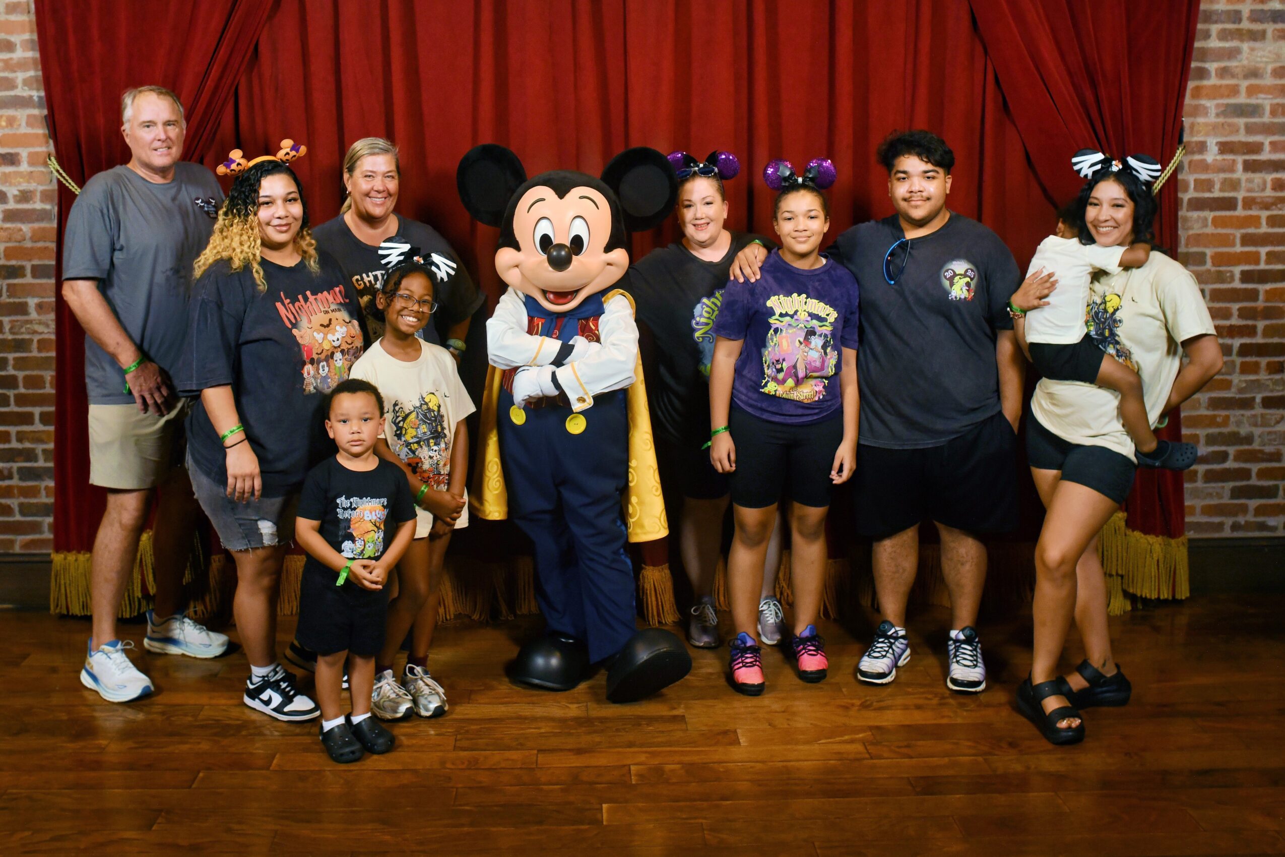 Group of nine people, including a person in Mickey Mouse costume, standing in front of red curtain, smiling.
