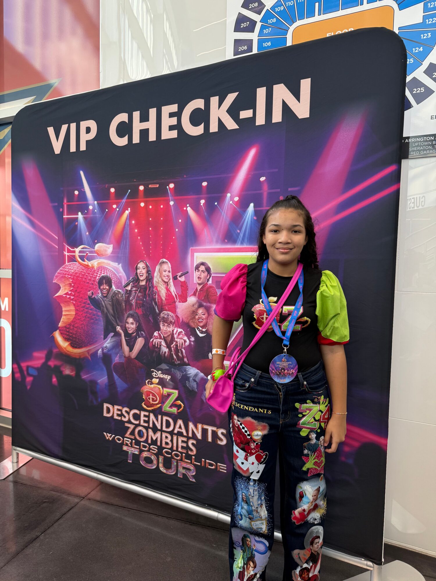 Young girl with a pink bag and green backpack standing next to a large digital screen at a nightclub event.