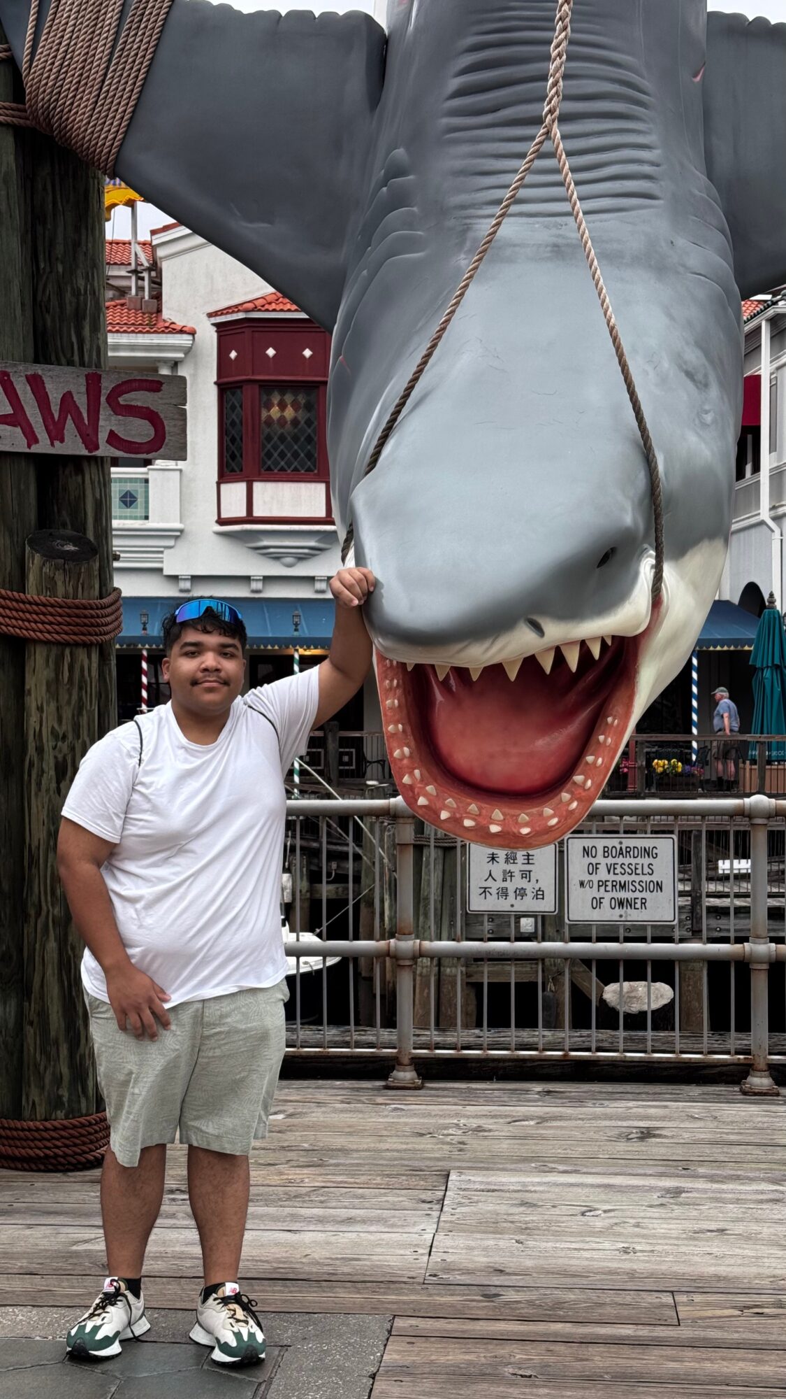 Person standing next to a large dinosaur head sculpture with open mouth, in an outdoor setting.