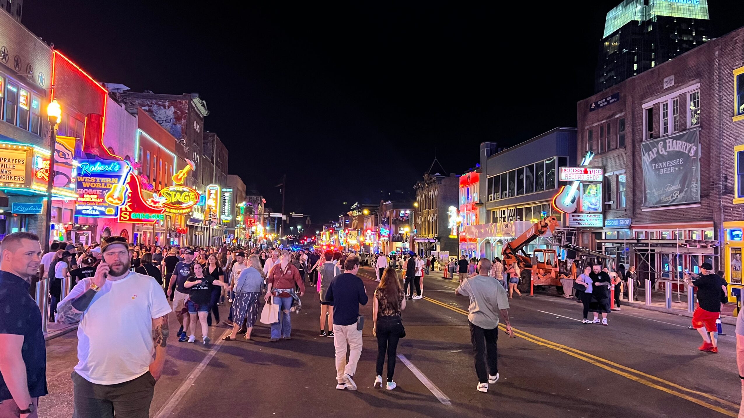 Night scene of a busy street with neon signs, people walking, and buildings on both sides.