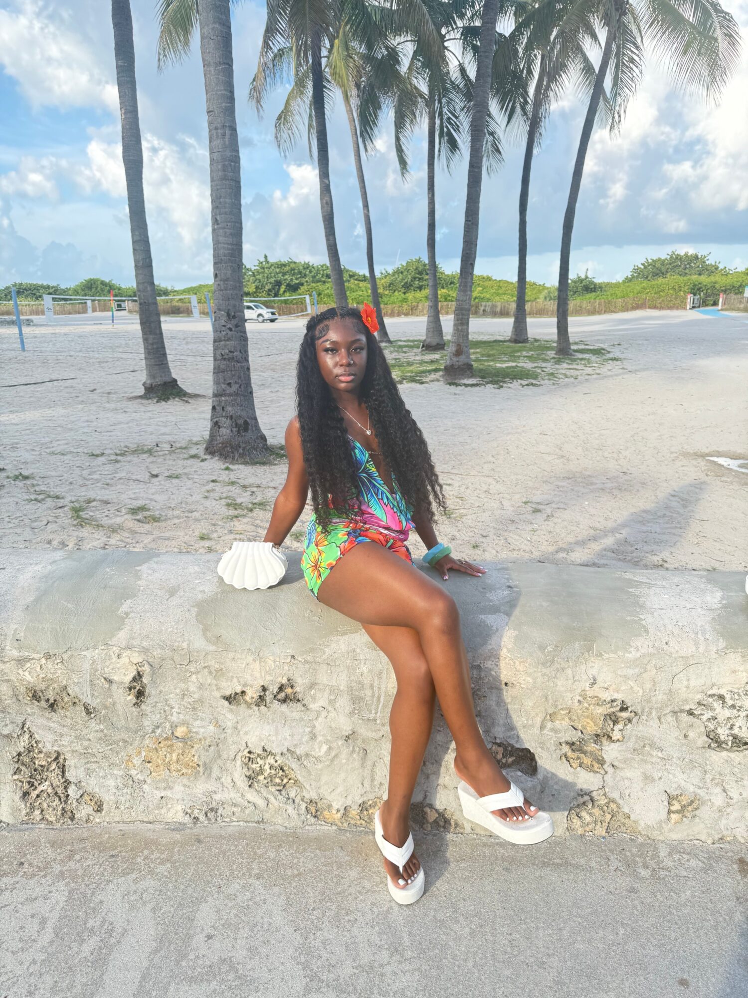Woman in colorful swimsuit and cover-up on beach with palm trees and ocean in background.
