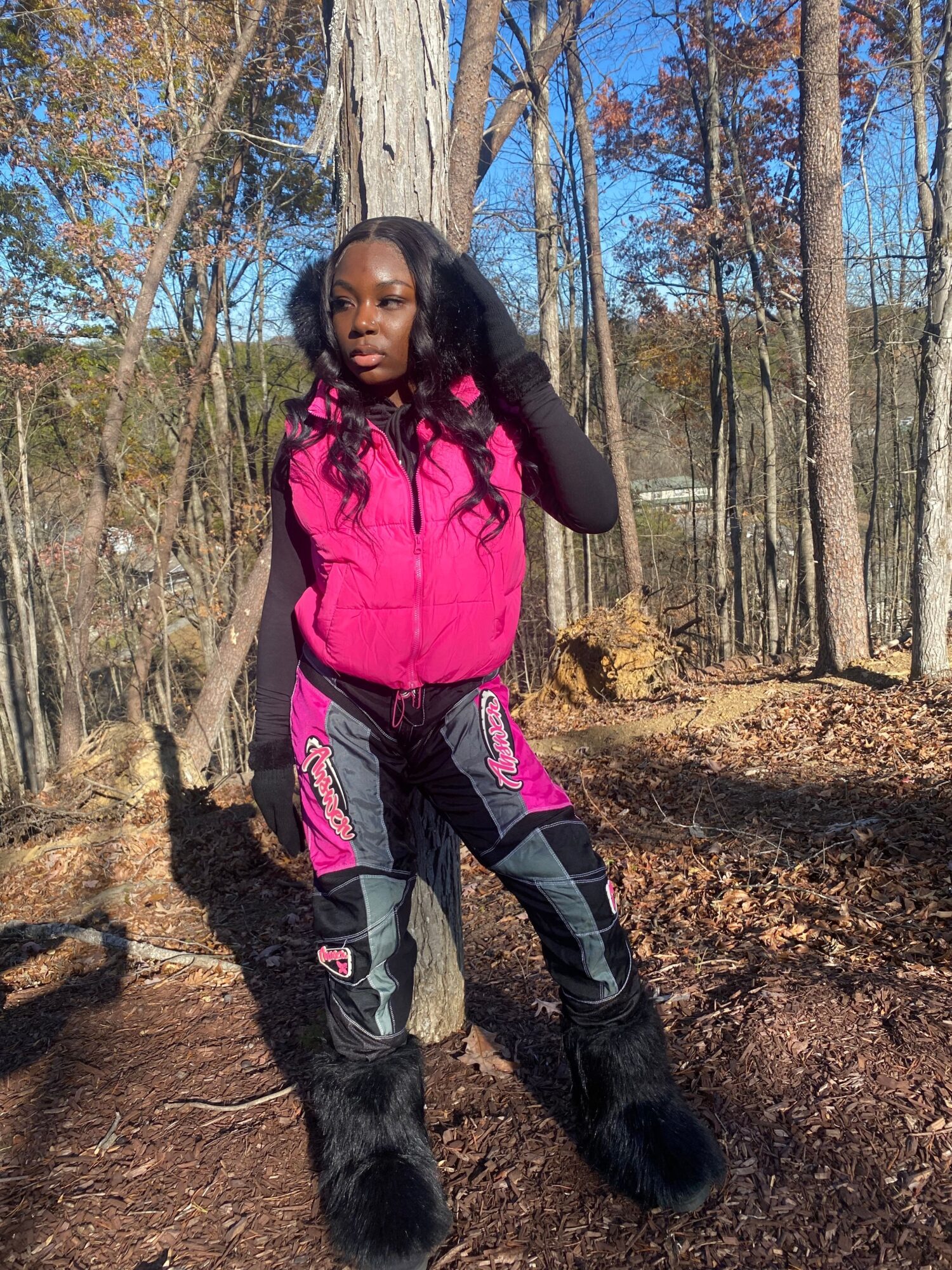 Woman in pink jacket and black pants walking on a forest trail with trees and blue sky in background.