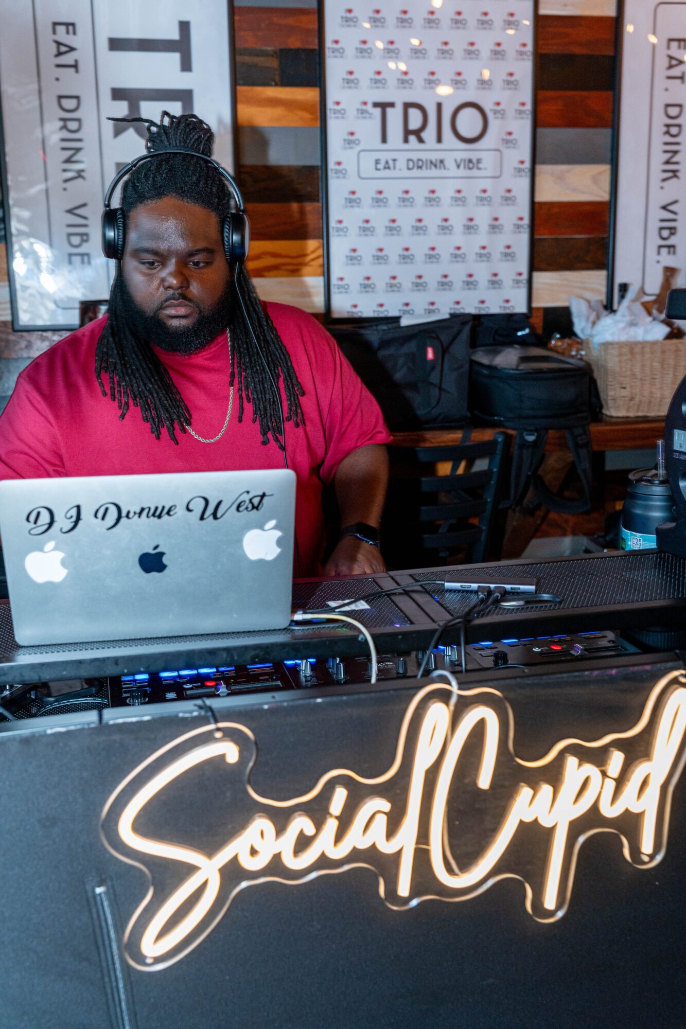 DJ with headphones working on a laptop at a social event, with signs and decorations in the background.