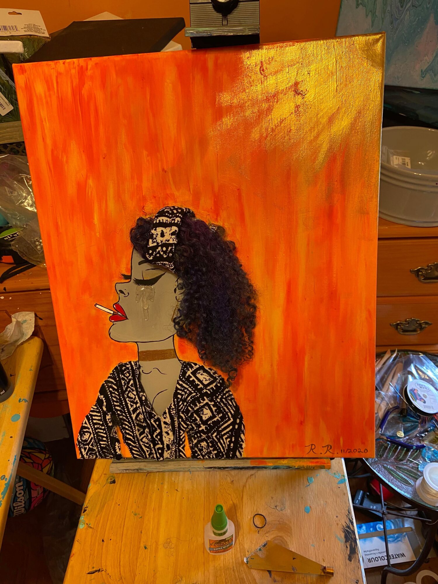 Portrait of a woman with curly hair, wearing glasses and patterned clothing, against an orange background.
