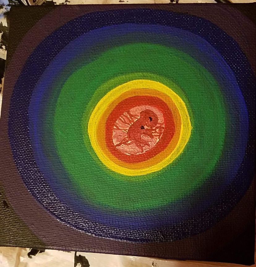 Colorful circular pattern with a central red area featuring a lion illustration, surrounded by yellow, green, blue, and purple rings.