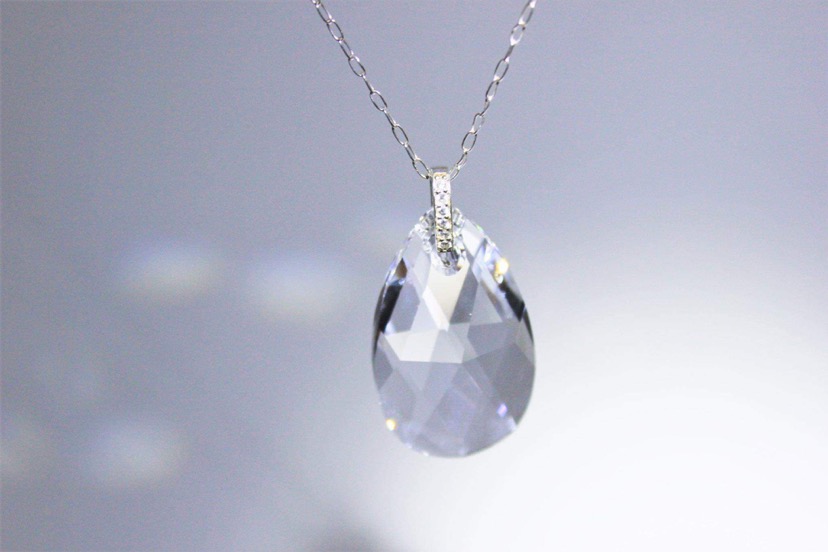 A teardrop-shaped crystal pendant necklace hangs from a chain against a light background.