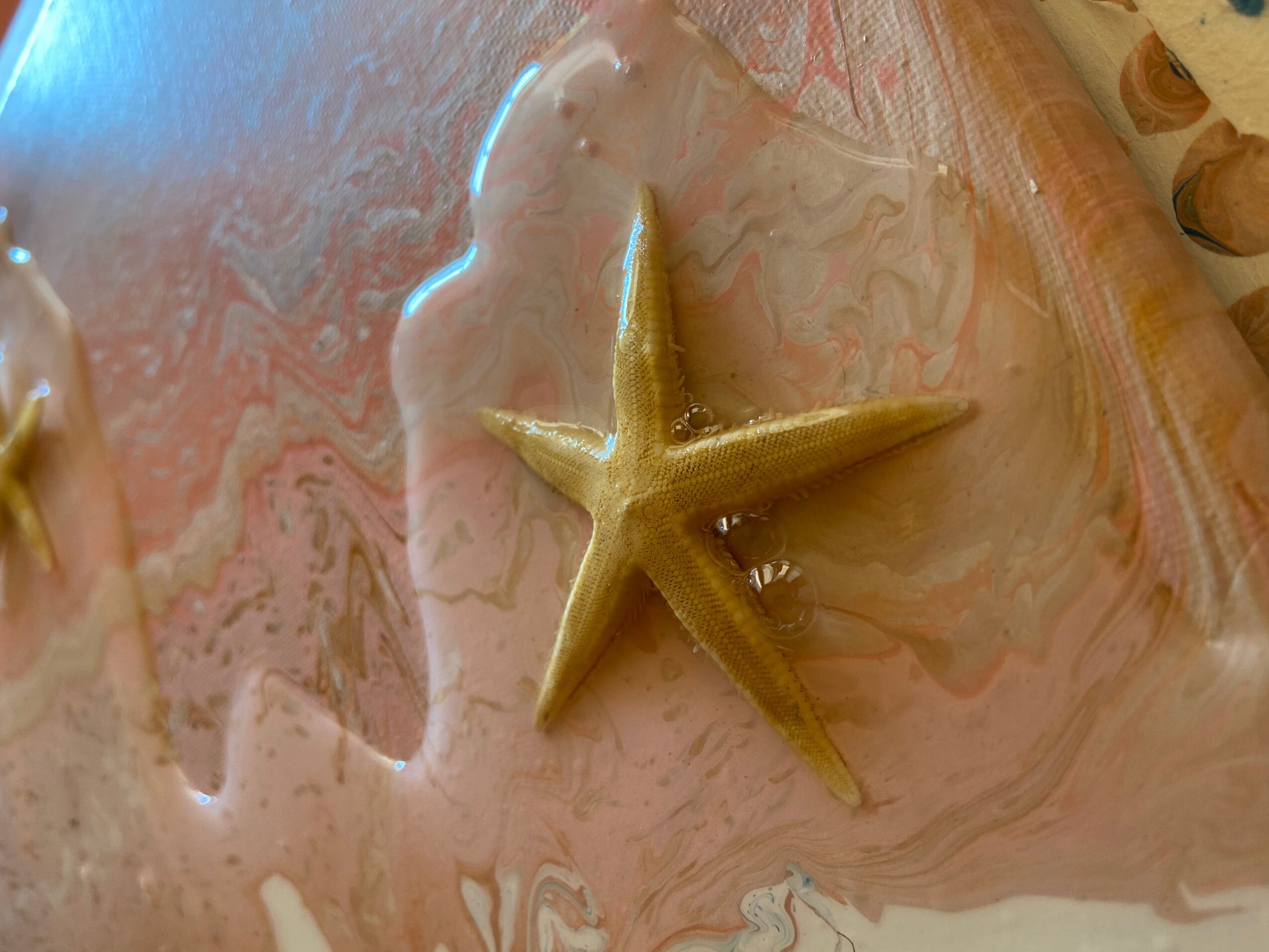 Starfish on a pink and beige marbled surface with water around it.