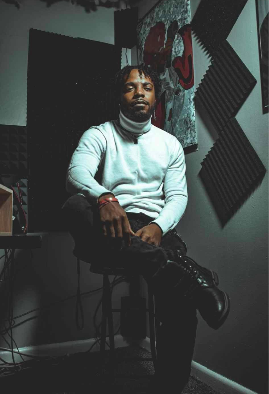 Person with dreadlocks sitting on a chair in a room with soundproofing foam panels and artwork on the wall.