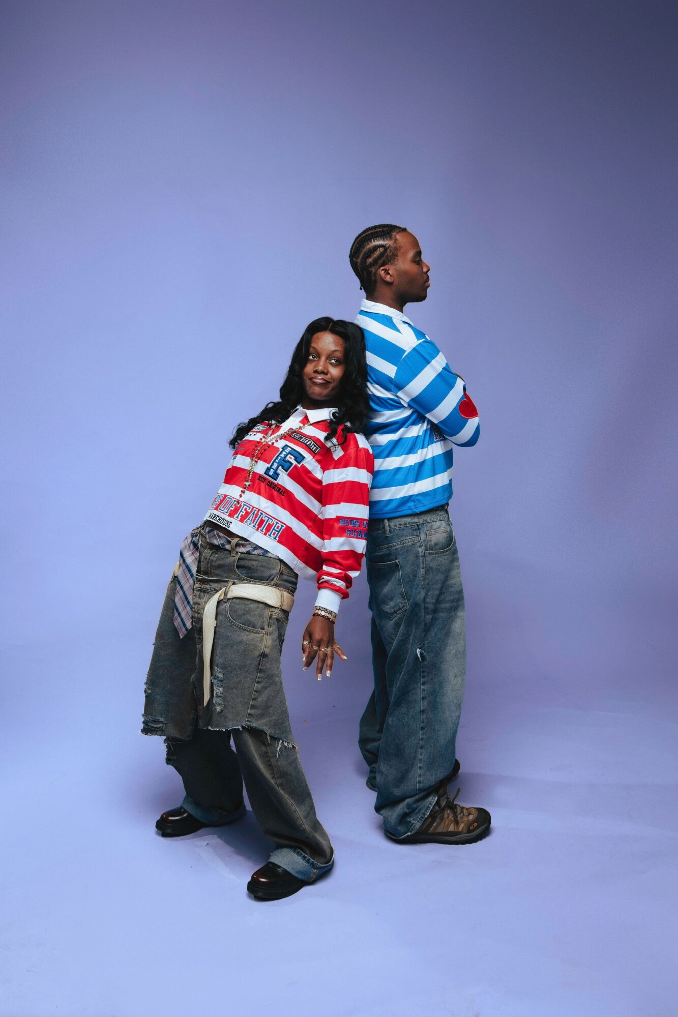 Two people standing back-to-back, one smiling and the other looking away, against a plain blue background.