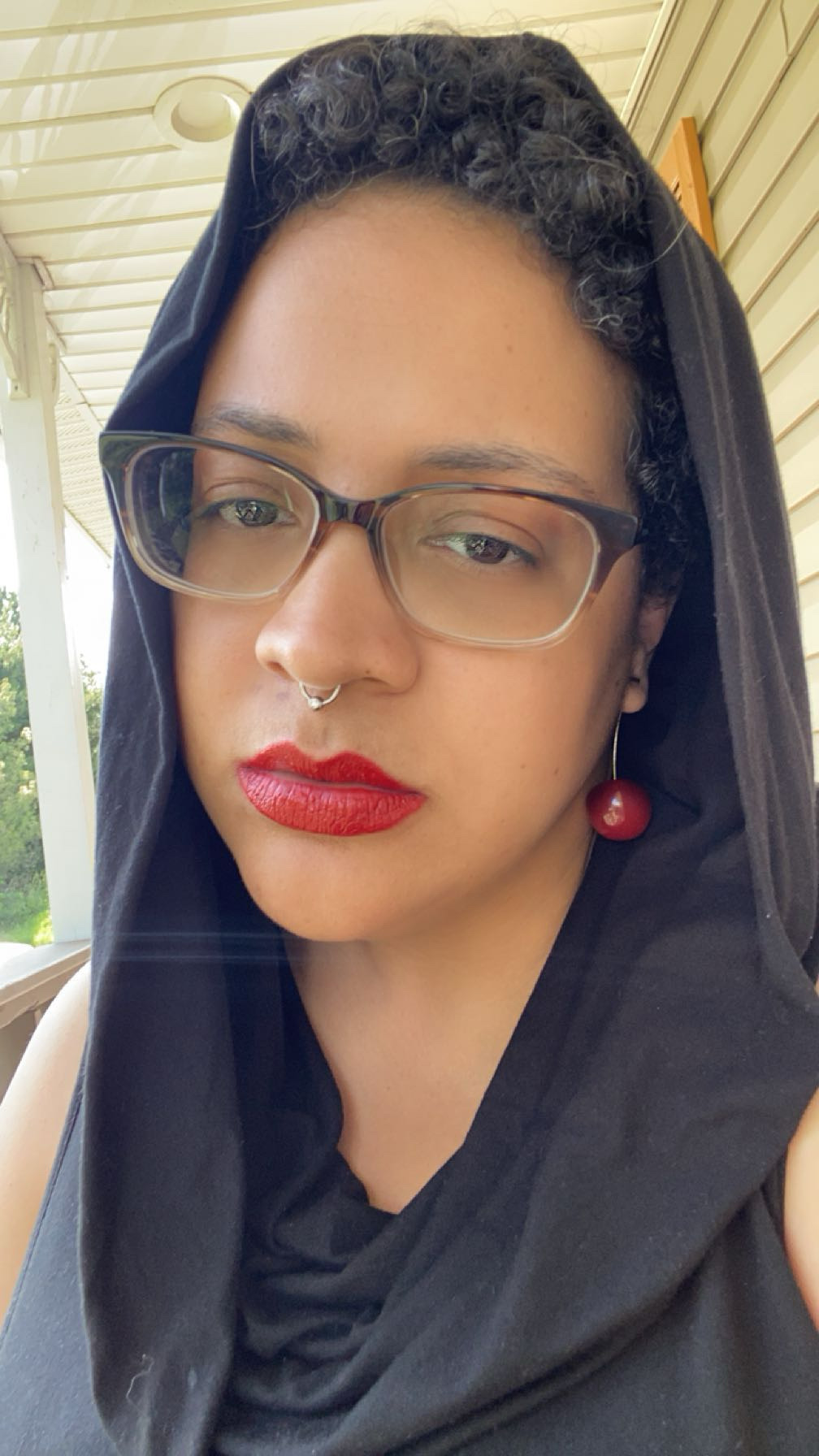 Person with glasses, red lipstick, and a black headscarf, looking directly at the camera.