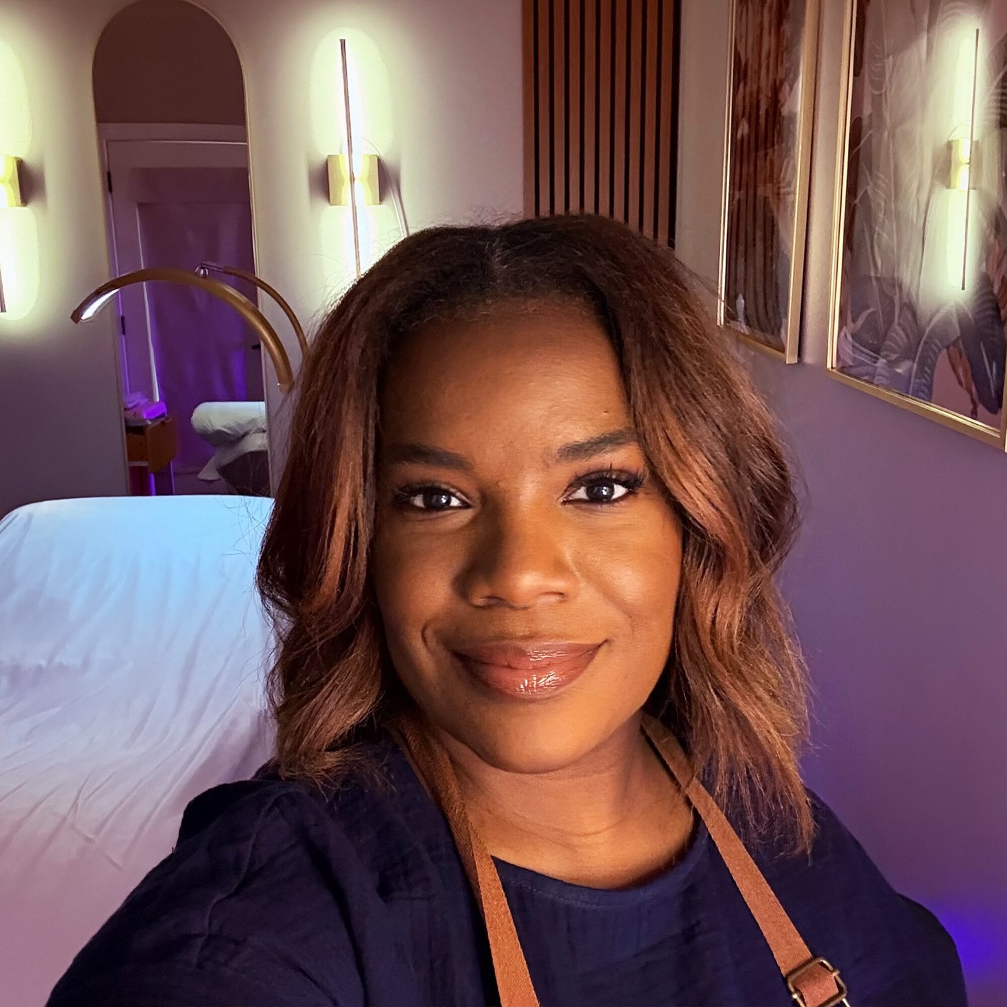 A woman with shoulder-length wavy hair smiling in a modern room with warm lighting and artwork.