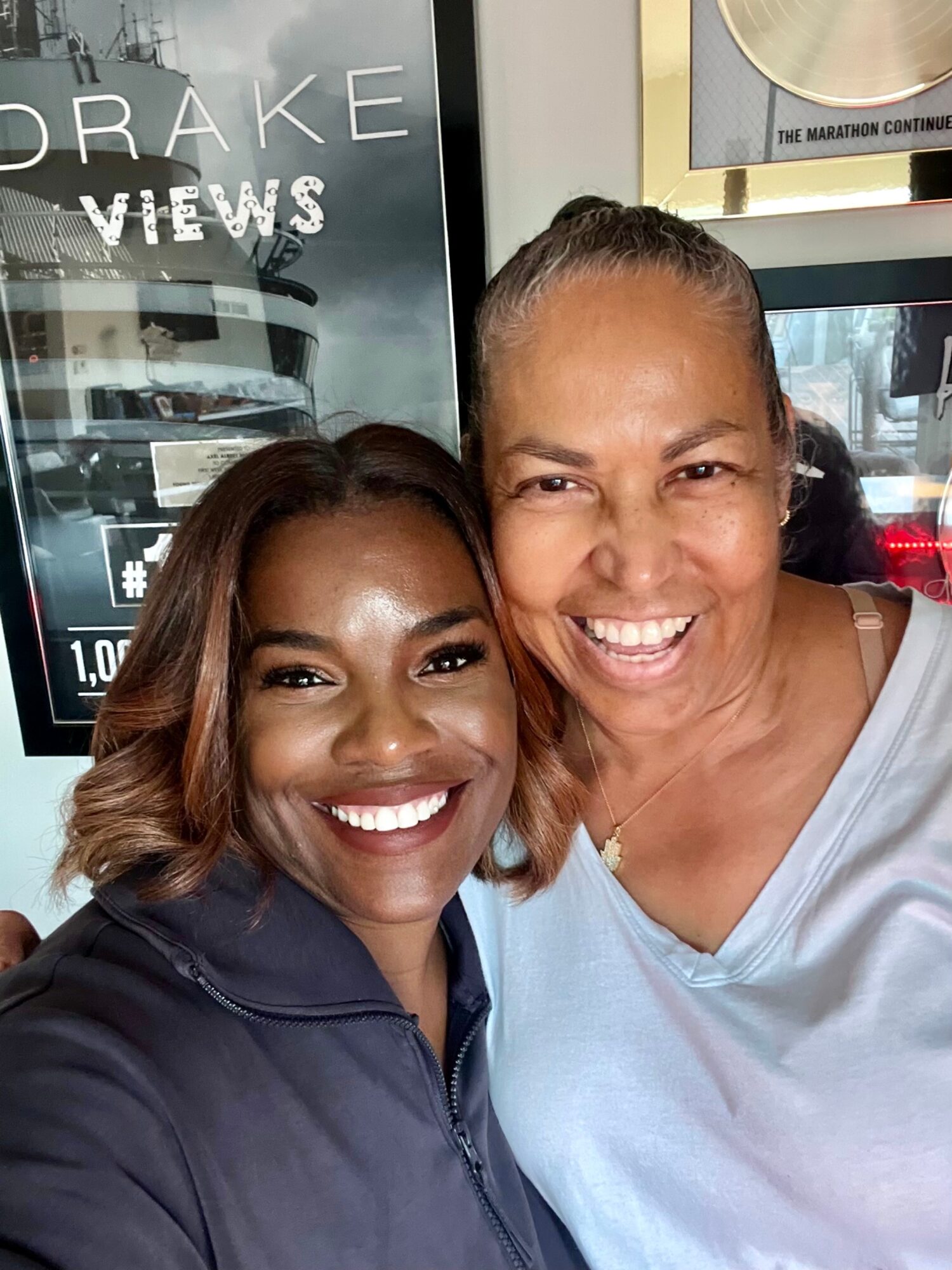 Two women smiling and taking a selfie indoors, with a sign and window in the background.