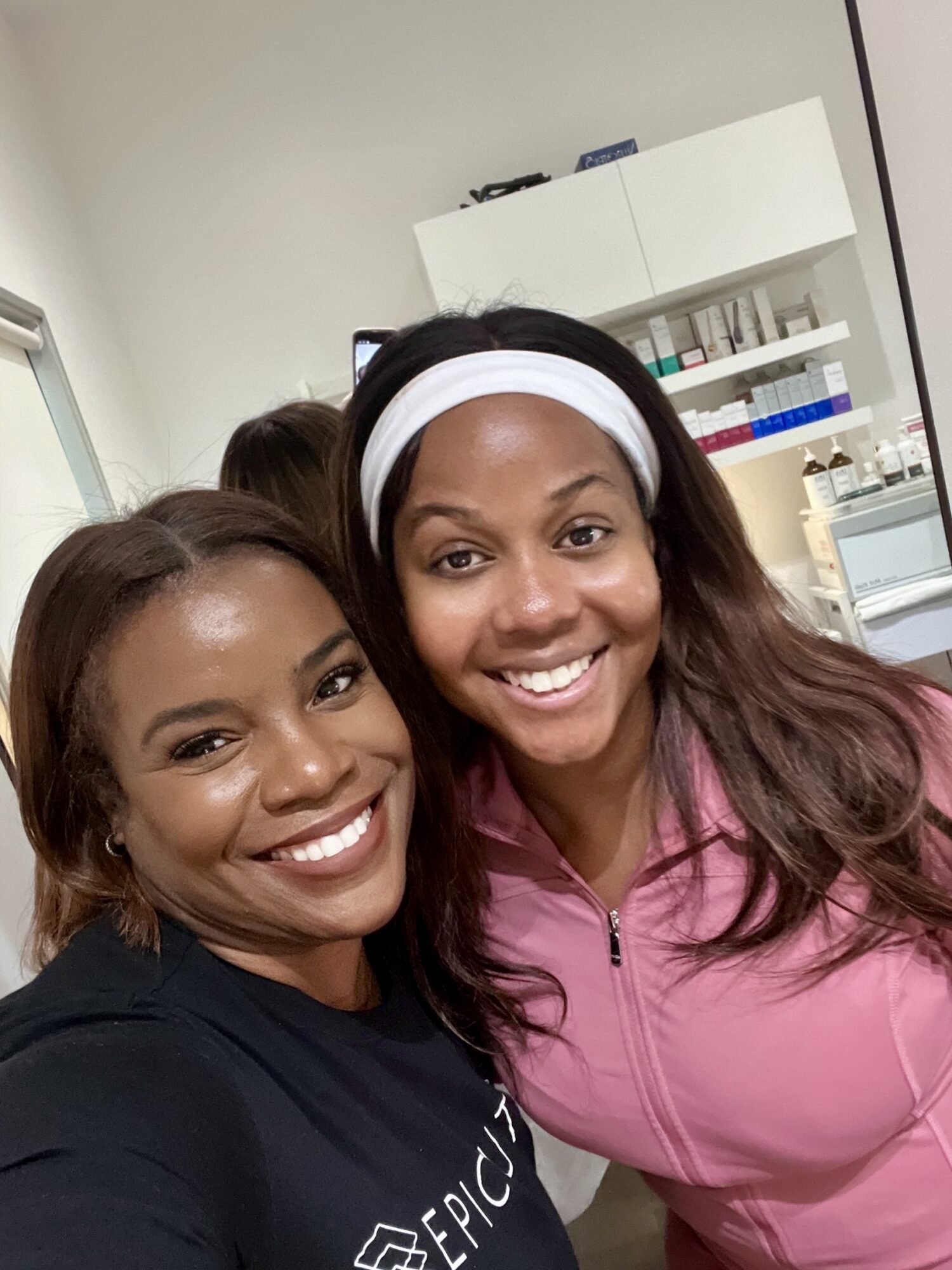 Two women smiling in a medical or laboratory setting, with shelves and equipment in the background.