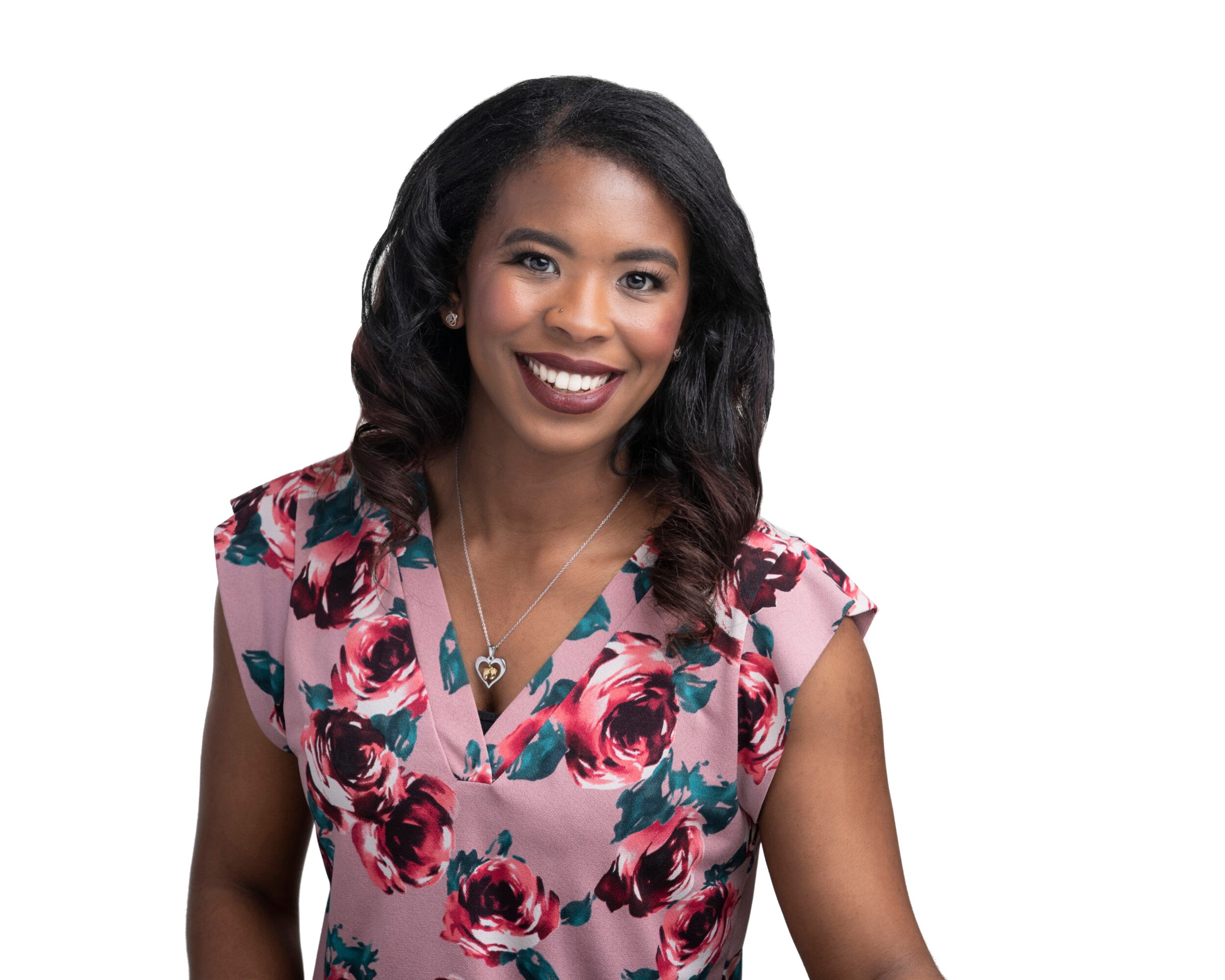Smiling woman with dark wavy hair wearing a floral top and a necklace, facing forward.