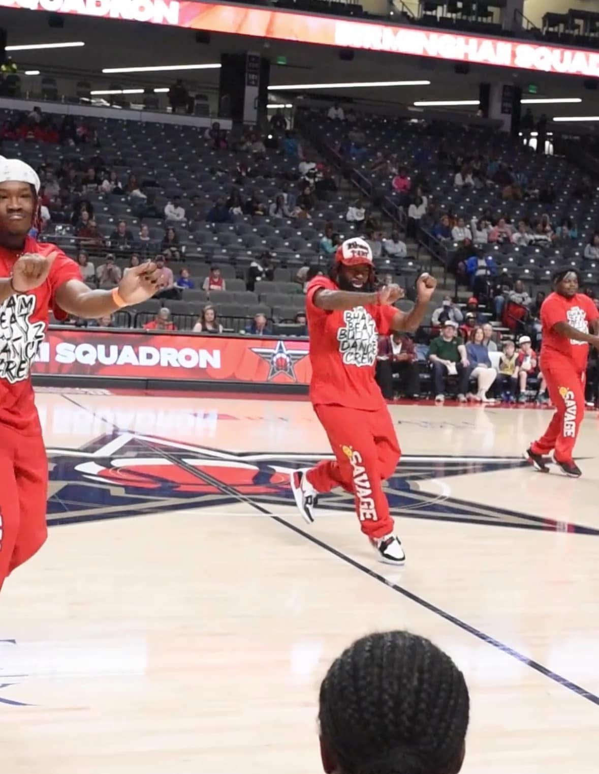 People dancing on a basketball court, wearing red outfits, with an empty arena in the background.