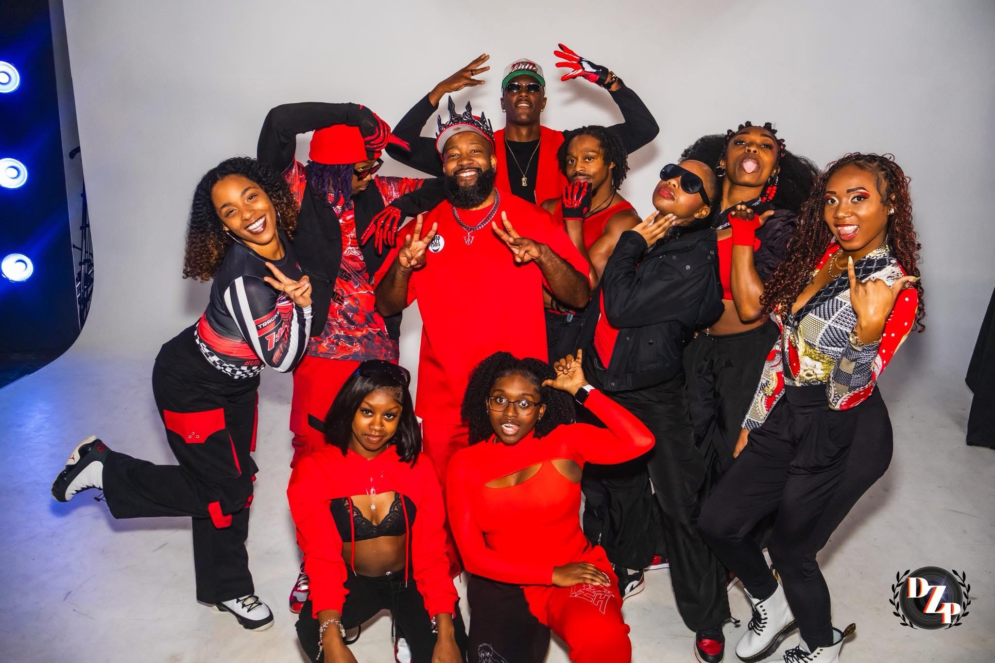 Group of ten people posing together, smiling, some making peace signs, in a studio with a plain background.