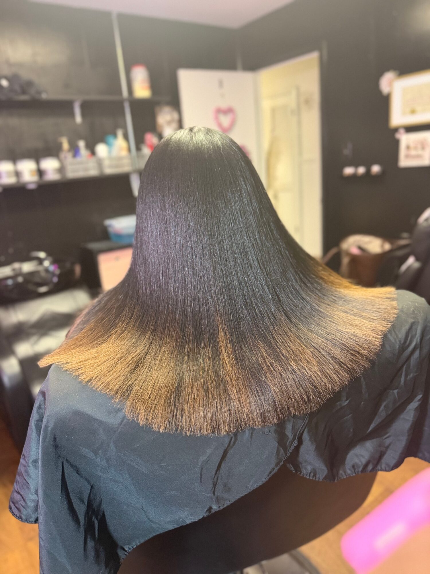 Person with straight, shoulder-length hair, dark at the top fading to lighter at the ends, sitting in a salon.