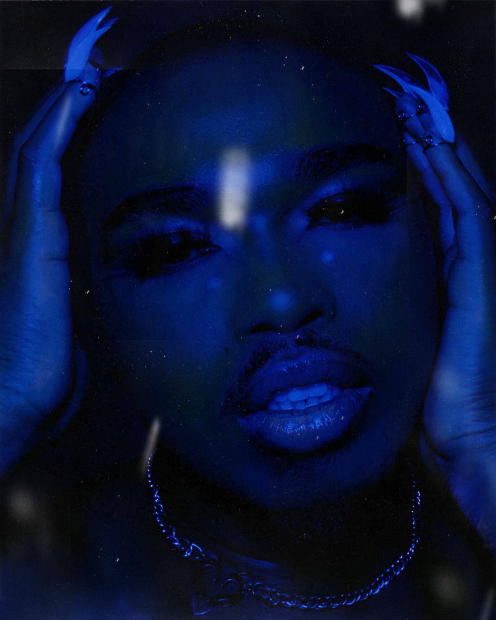 Close-up of a woman's face illuminated in blue light, with hands on her head, dark background, jewelry visible.