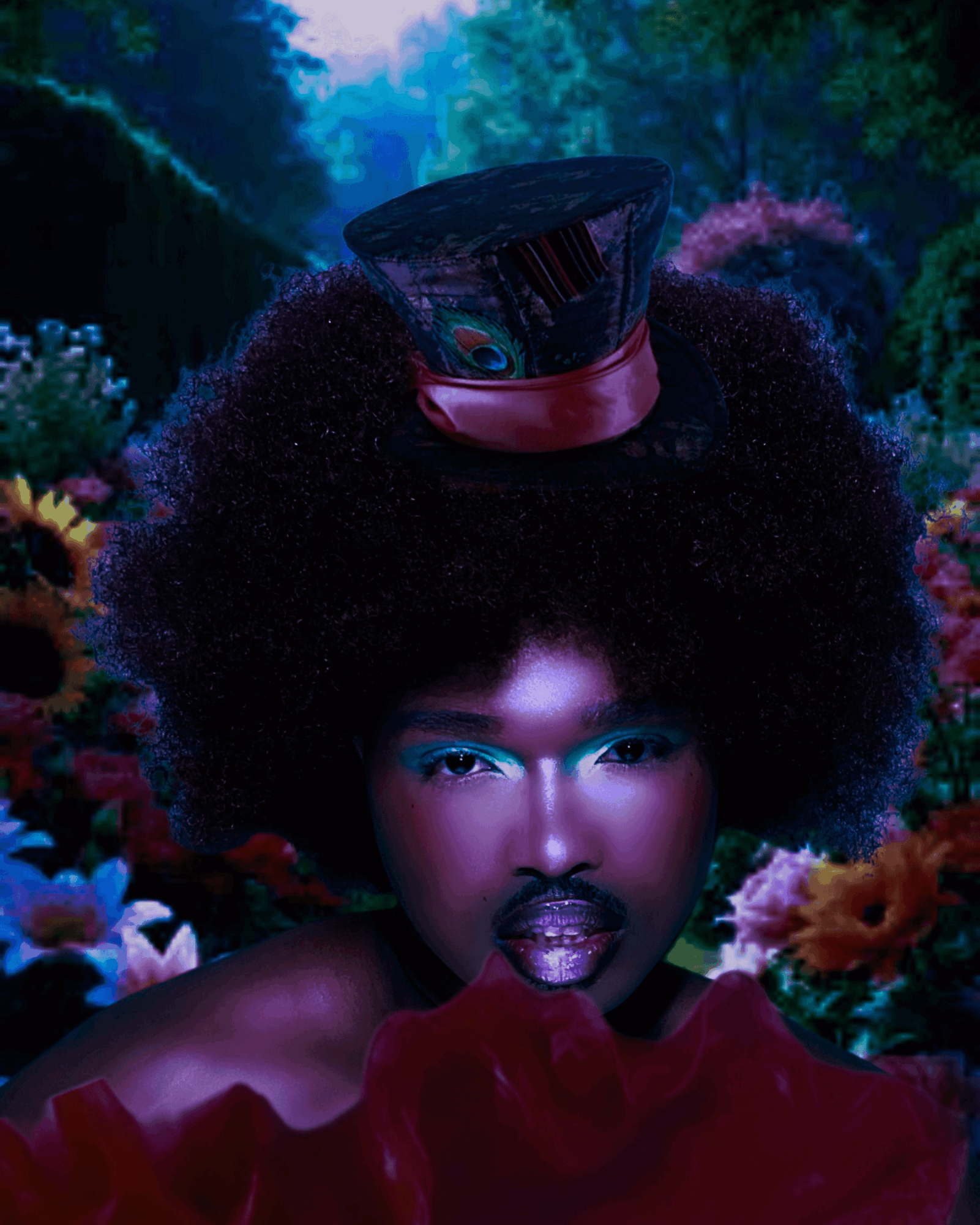 Portrait of a person with an afro hairstyle wearing a top hat, surrounded by colorful flowers in a garden.