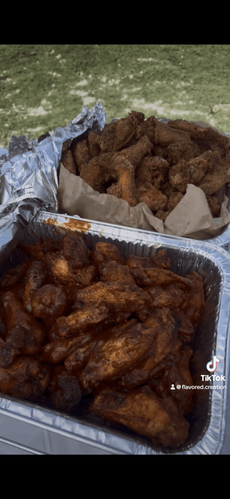Two trays of fried chicken, one with dark glazed pieces and the other with lighter, crispy pieces, on a grassy surface.