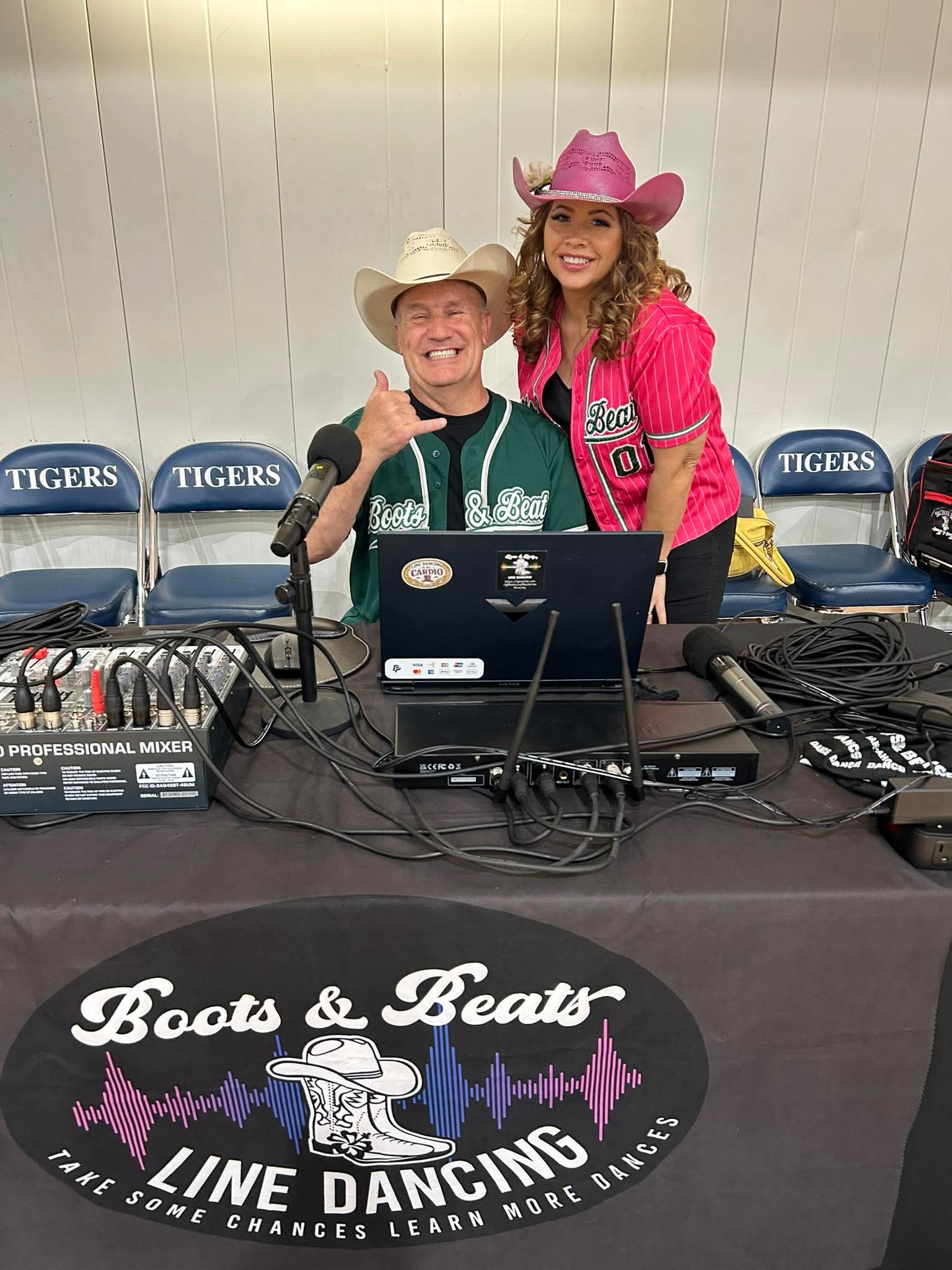 Two women wearing cowboy hats smiling behind DJ equipment at Boots & Beats Line Dancing event.