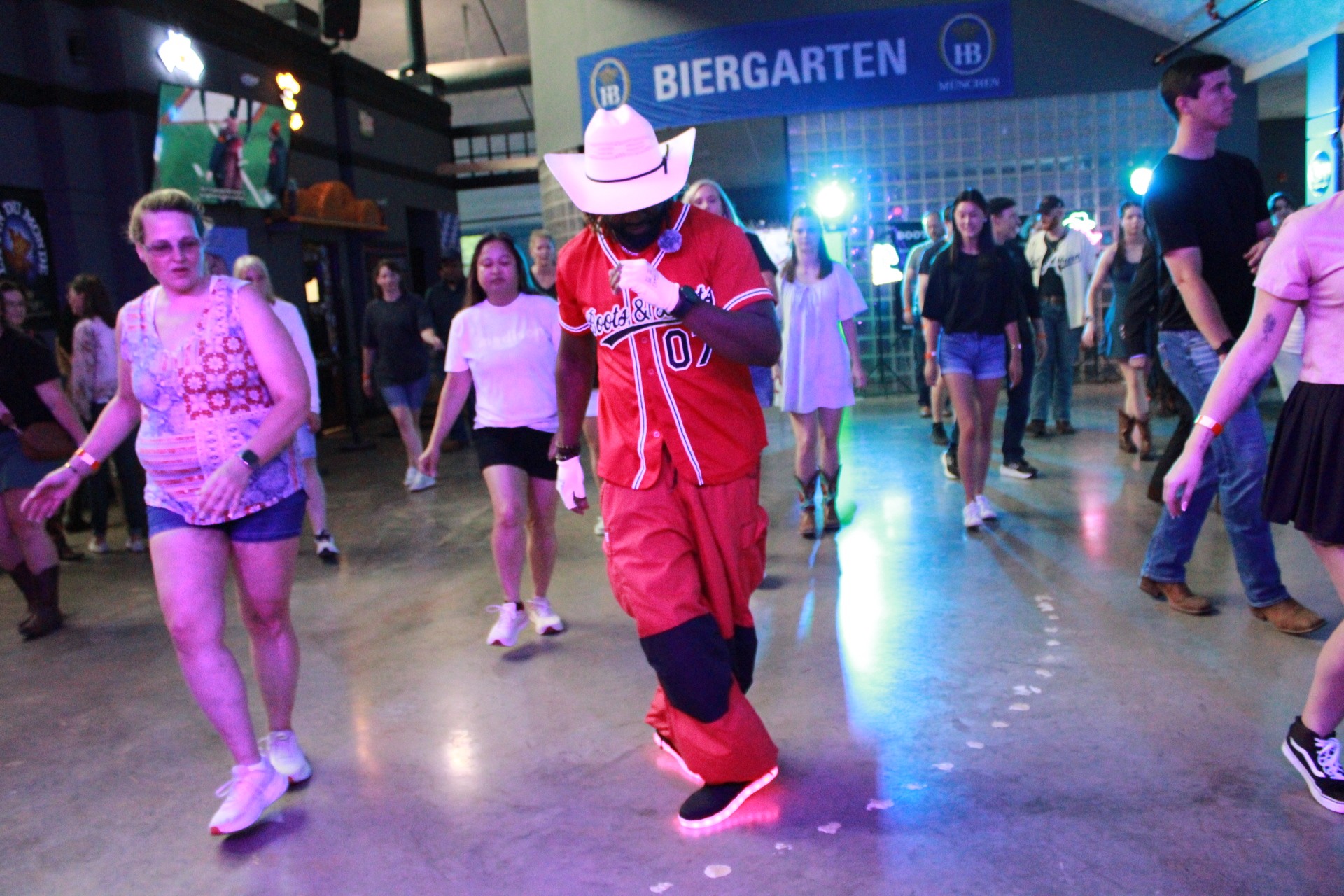 People dancing in a venue with a sign reading 'Biergarten' in the background, some wearing casual clothing and hats.