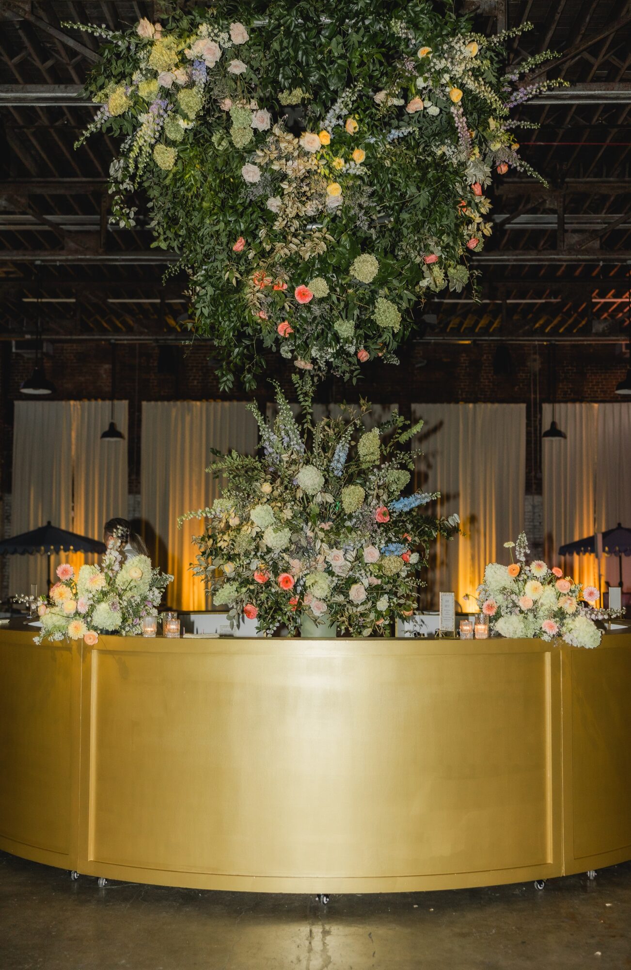 Decorative floral arrangement with hanging flowers above a gold-colored bar or counter, illuminated by warm lighting.